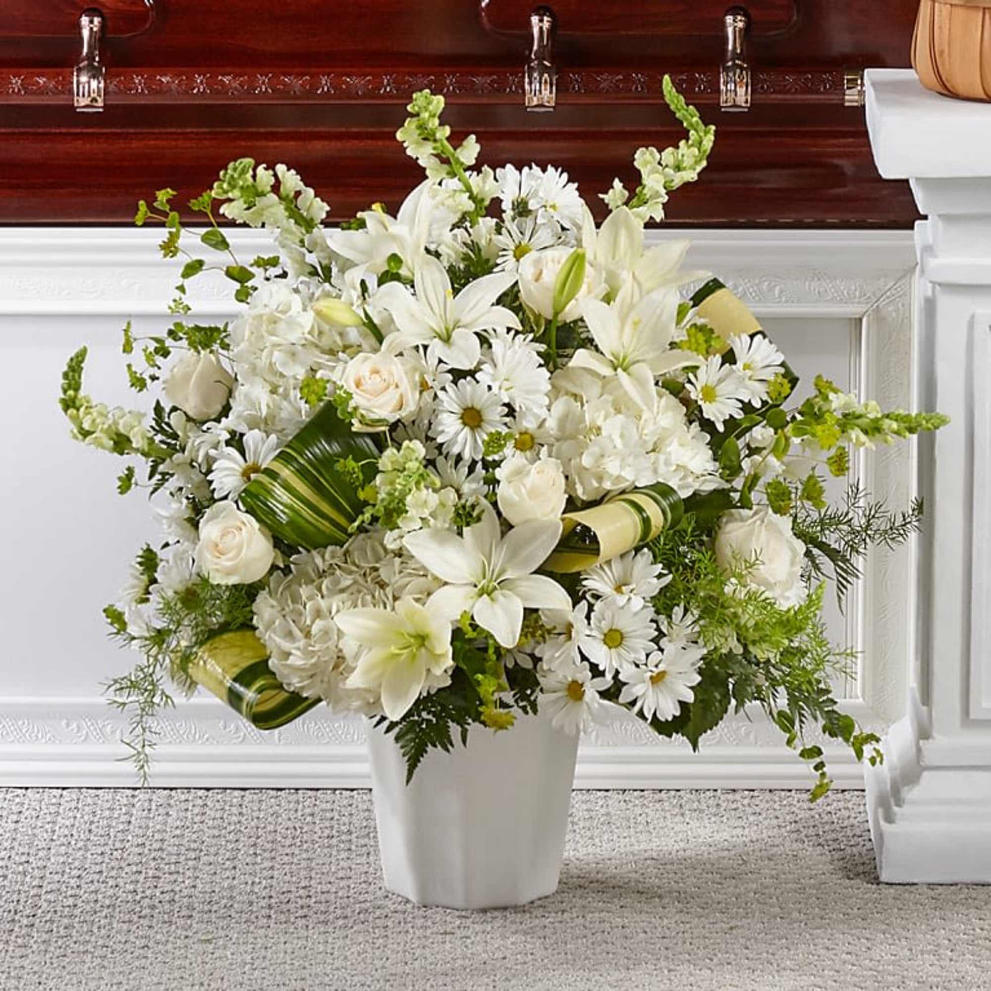 Tall white sympathy arrangement with lilies, roses, daisies, and hydrangeas in a white vase