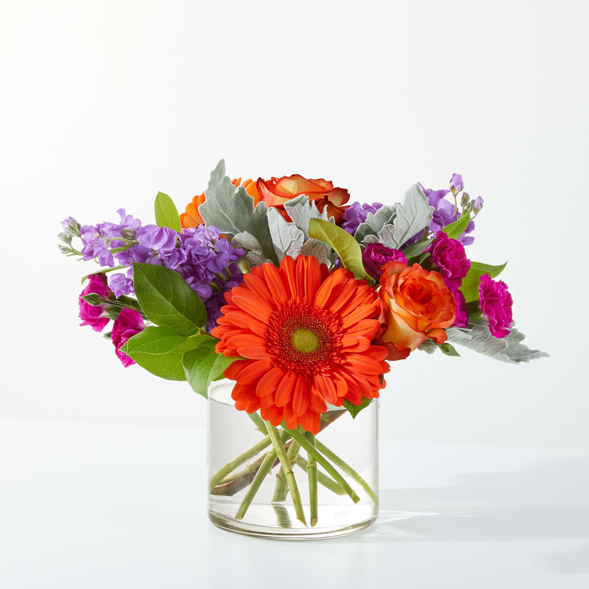 Orange gerbera daisies and roses in a clear glass vase