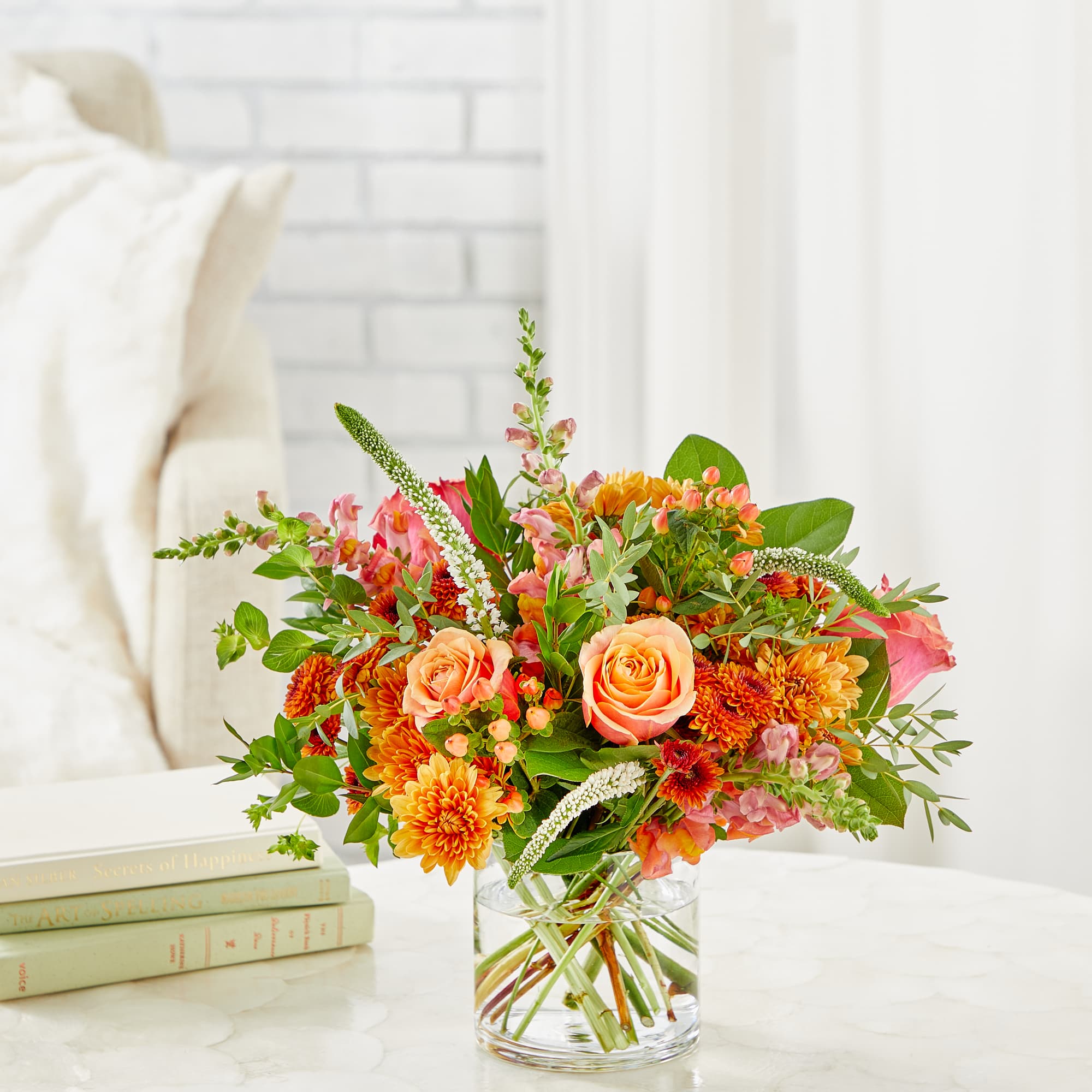 Mixed orange and pink flowers in a clear glass vase on a table