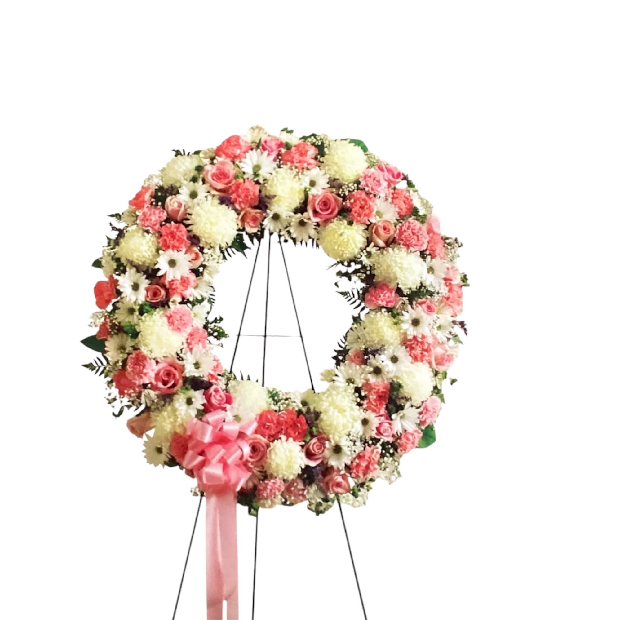 Large floral wreath on a stand with pink and white flowers and a pink ribbon