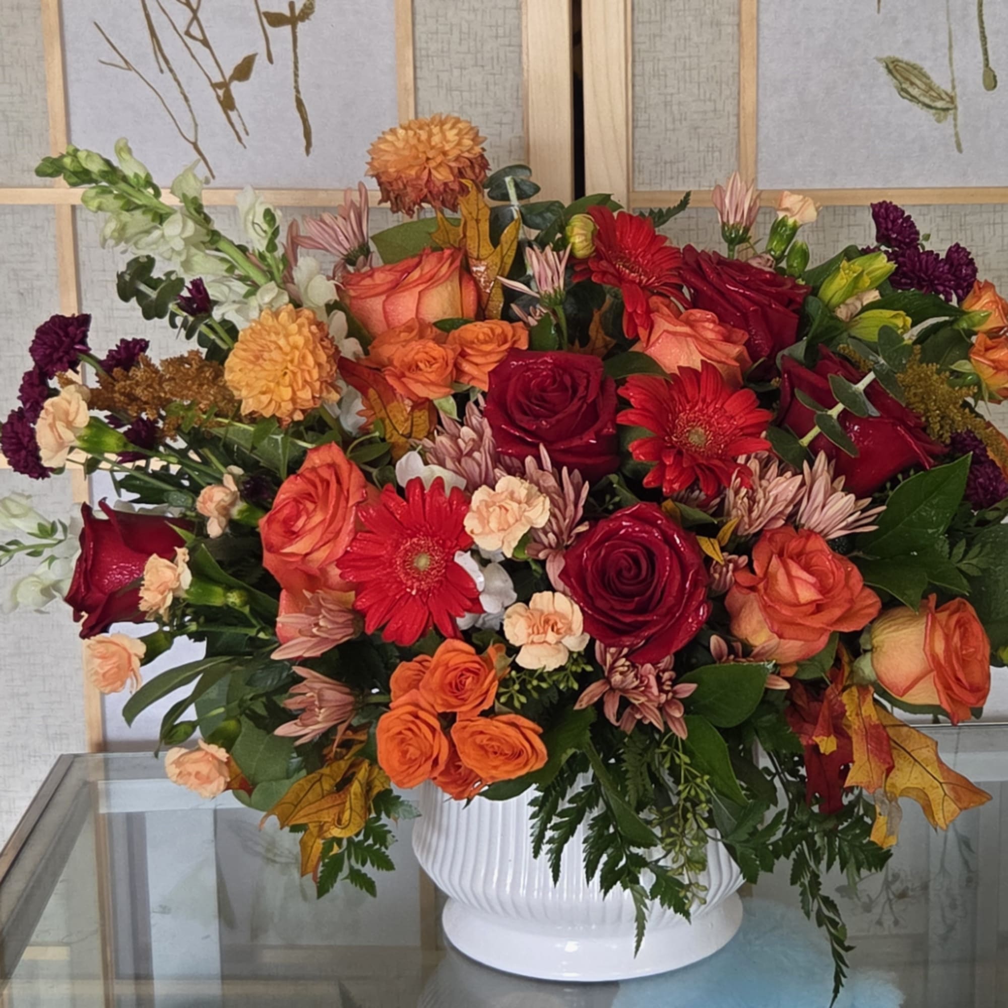 Mixed bouquet of red, orange, and peach flowers in a white vase, photo 2 of 4