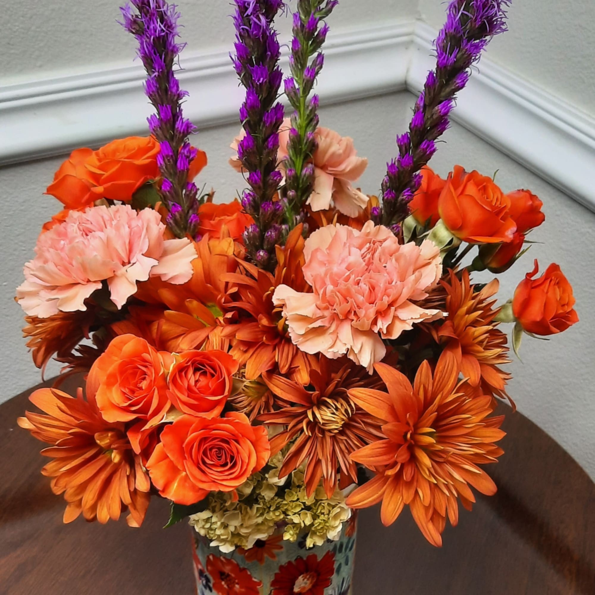 Orange and pink floral arrangement in a patterned vase with purple spikes