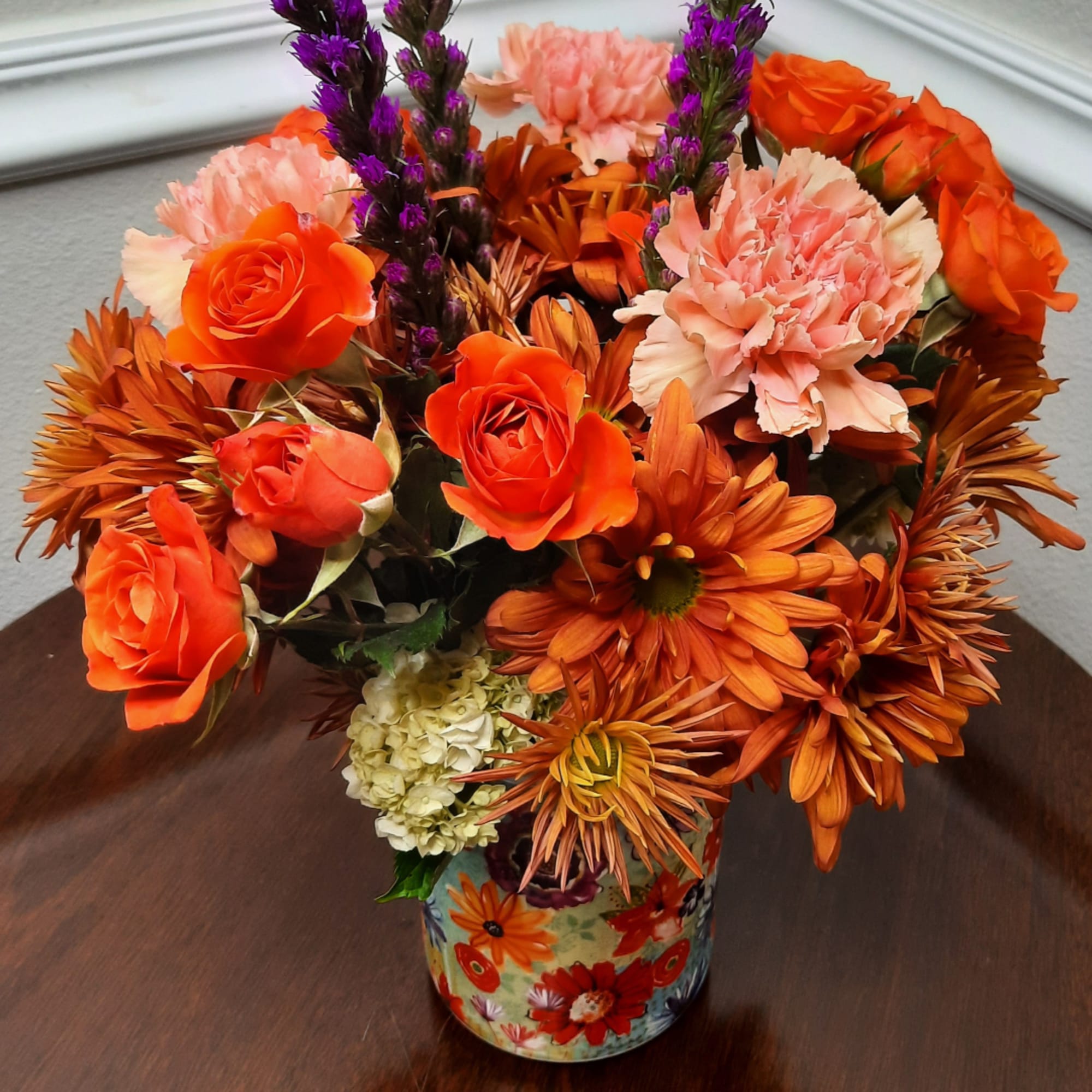Orange and pink floral arrangement in a patterned vase