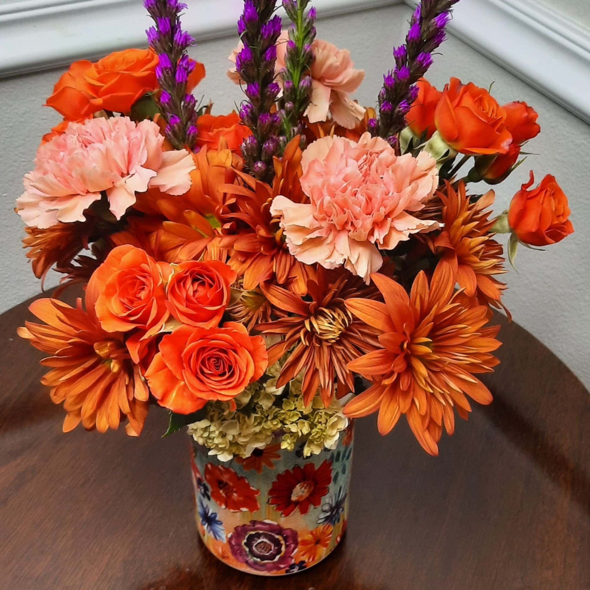Orange and pink flowers arranged in a patterned vase