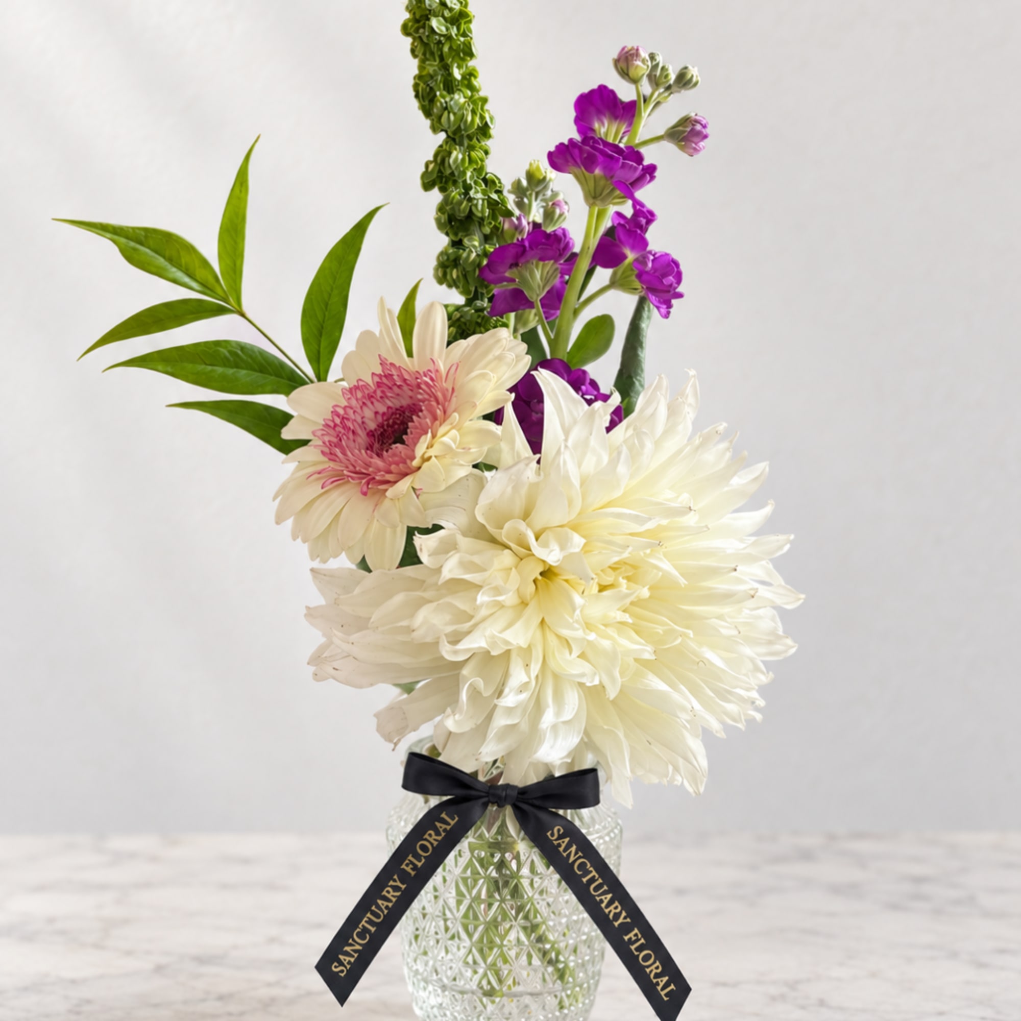 White and purple flowers arranged in a glass vase with a black ribbon