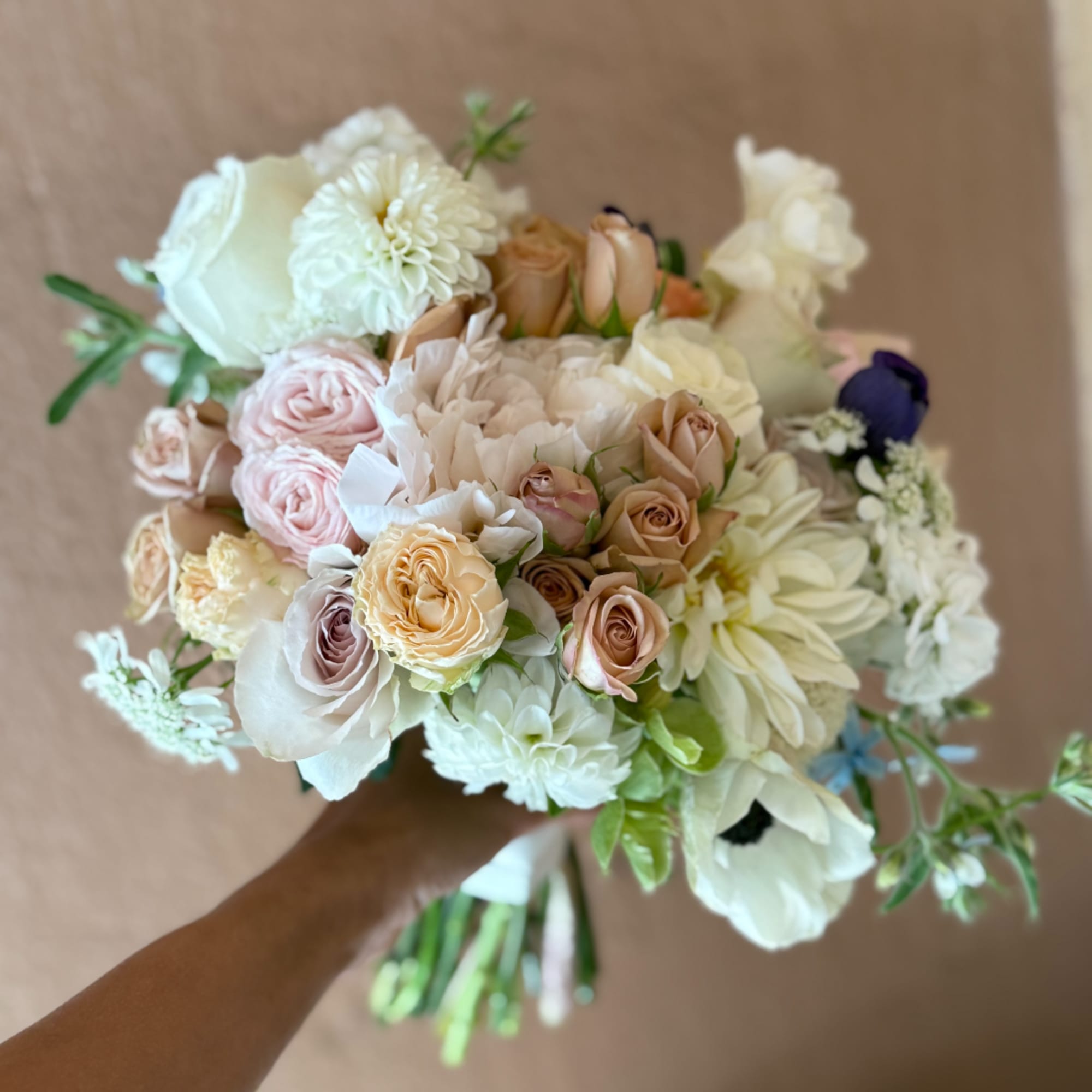 Handheld bouquet of blush, cream, and white flowers with a few pale peach blooms