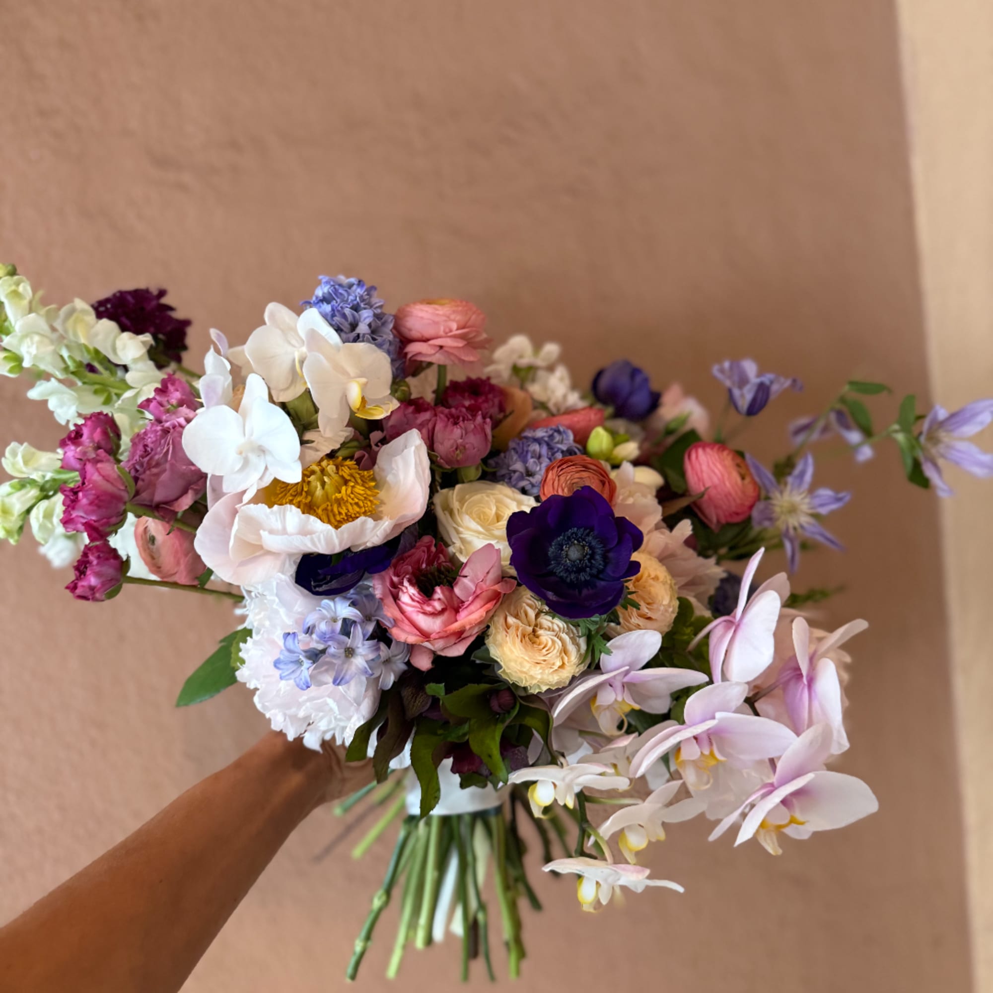 Handheld bouquet of mixed pastel and deep-toned flowers with orchids and ranunculus