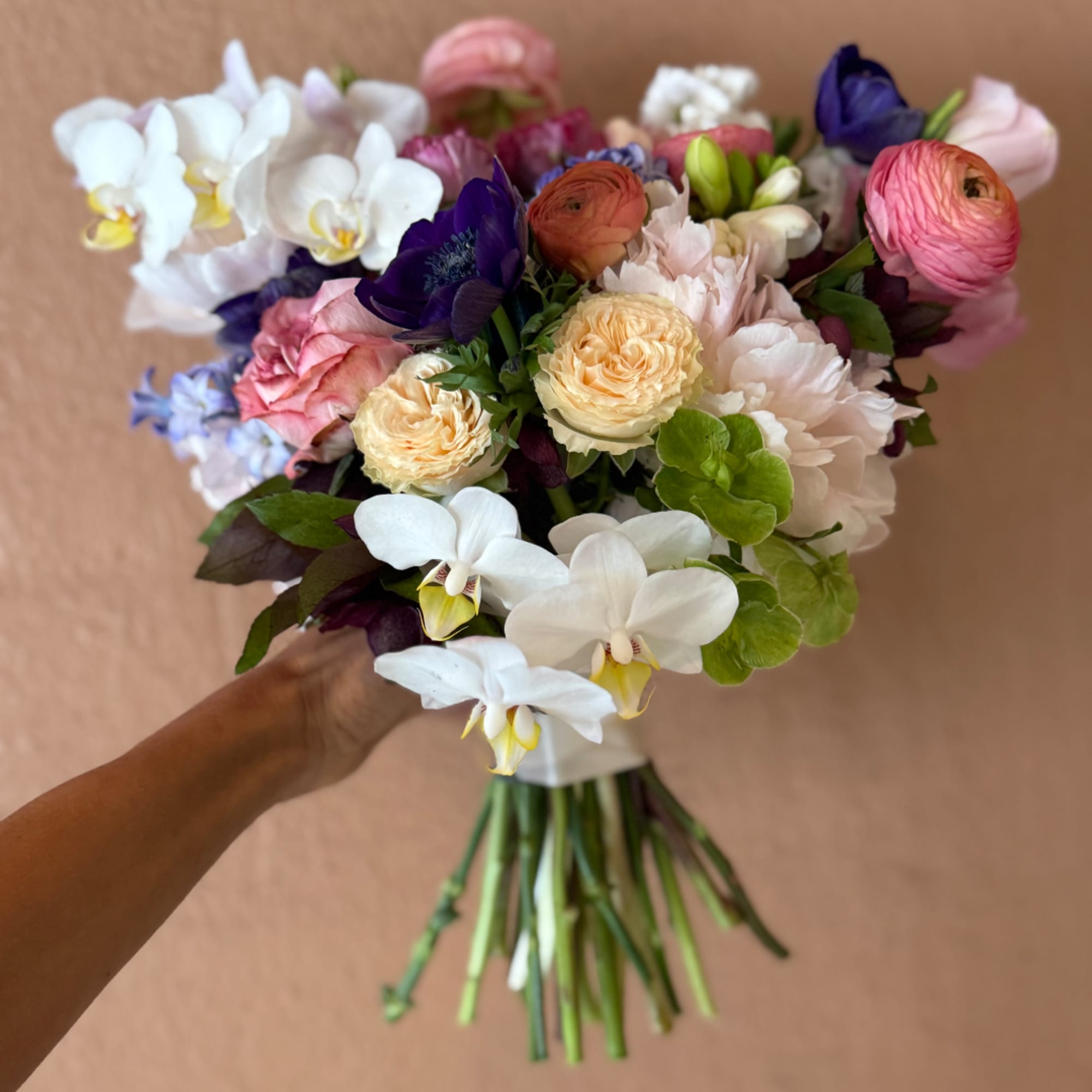 Handheld bouquet of white orchids, pink and cream blooms, and purple flowers