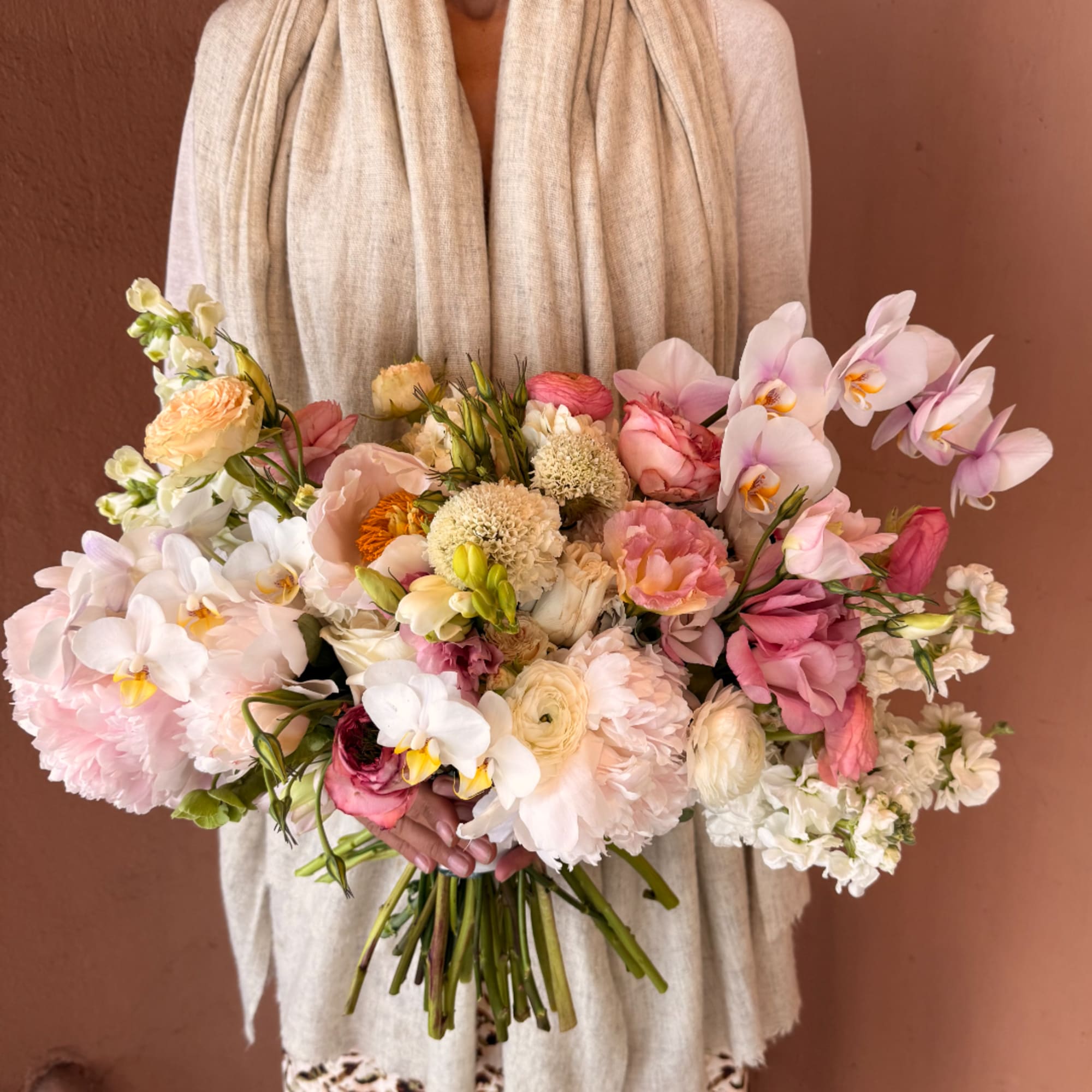 Handheld bouquet of blush, white, and peach flowers with orchids