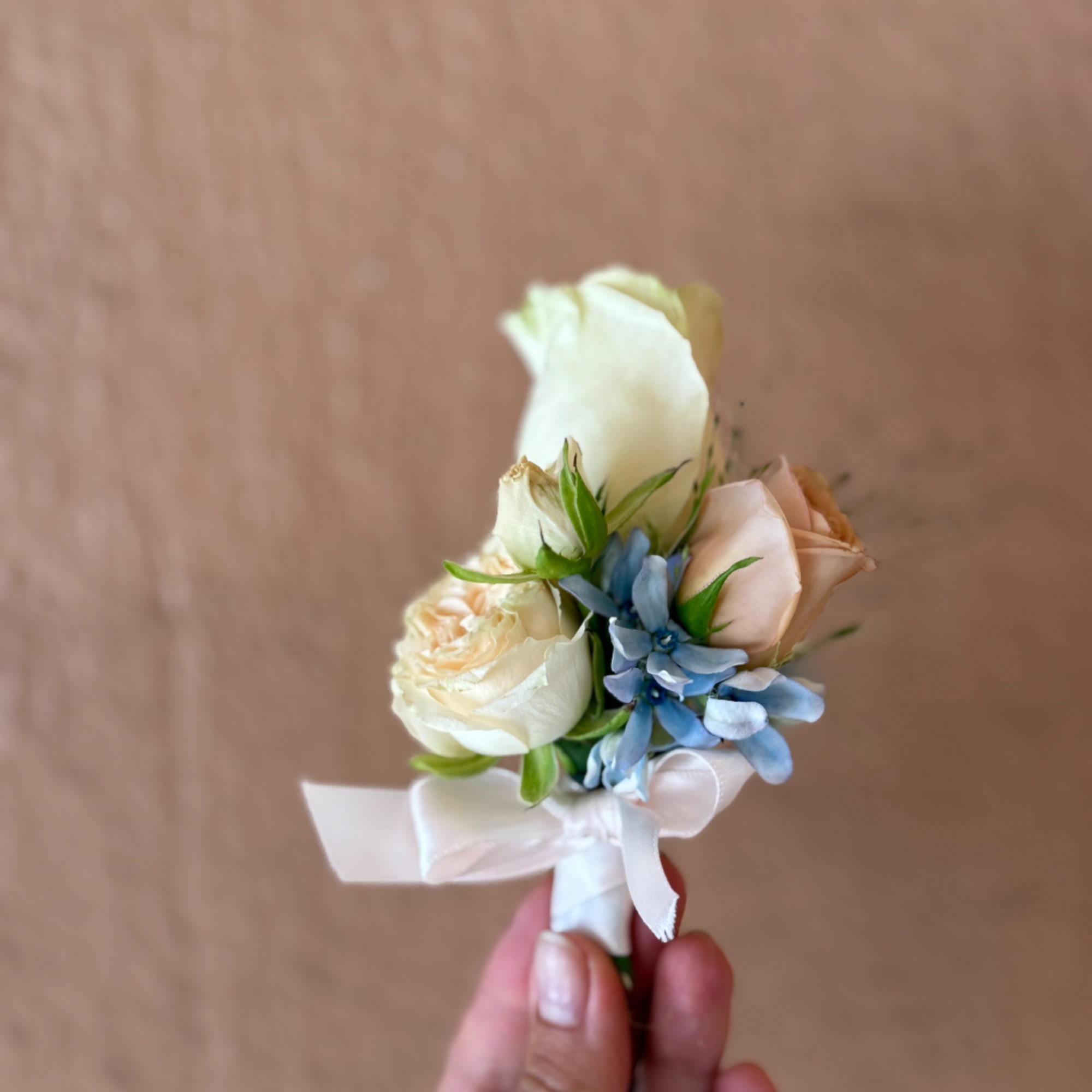 Small wedding boutonniere with cream roses and blue flowers tied with white ribbon