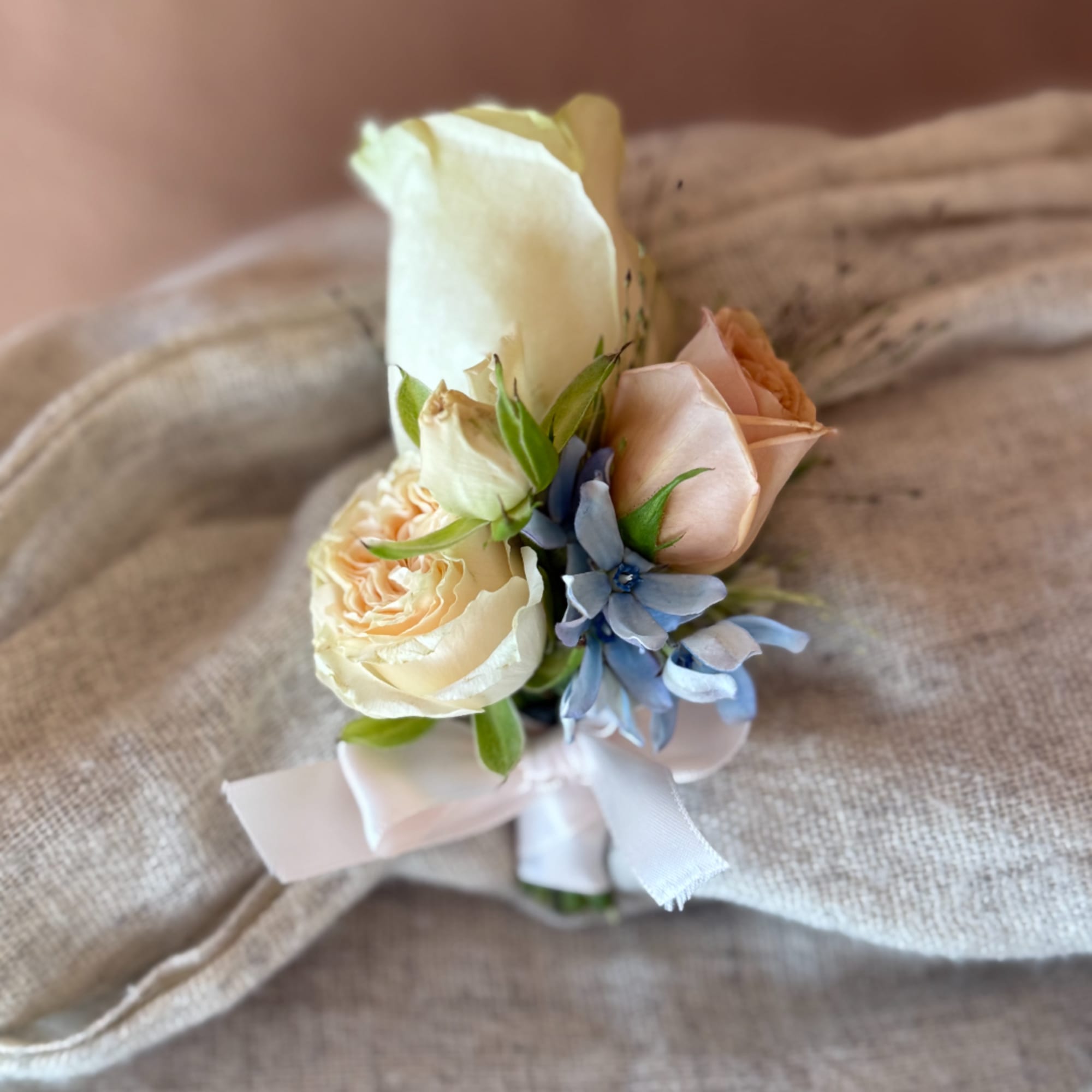 Small bridal bouquet with cream roses, pale peach blooms, and blue flowers tied with white ribbon
