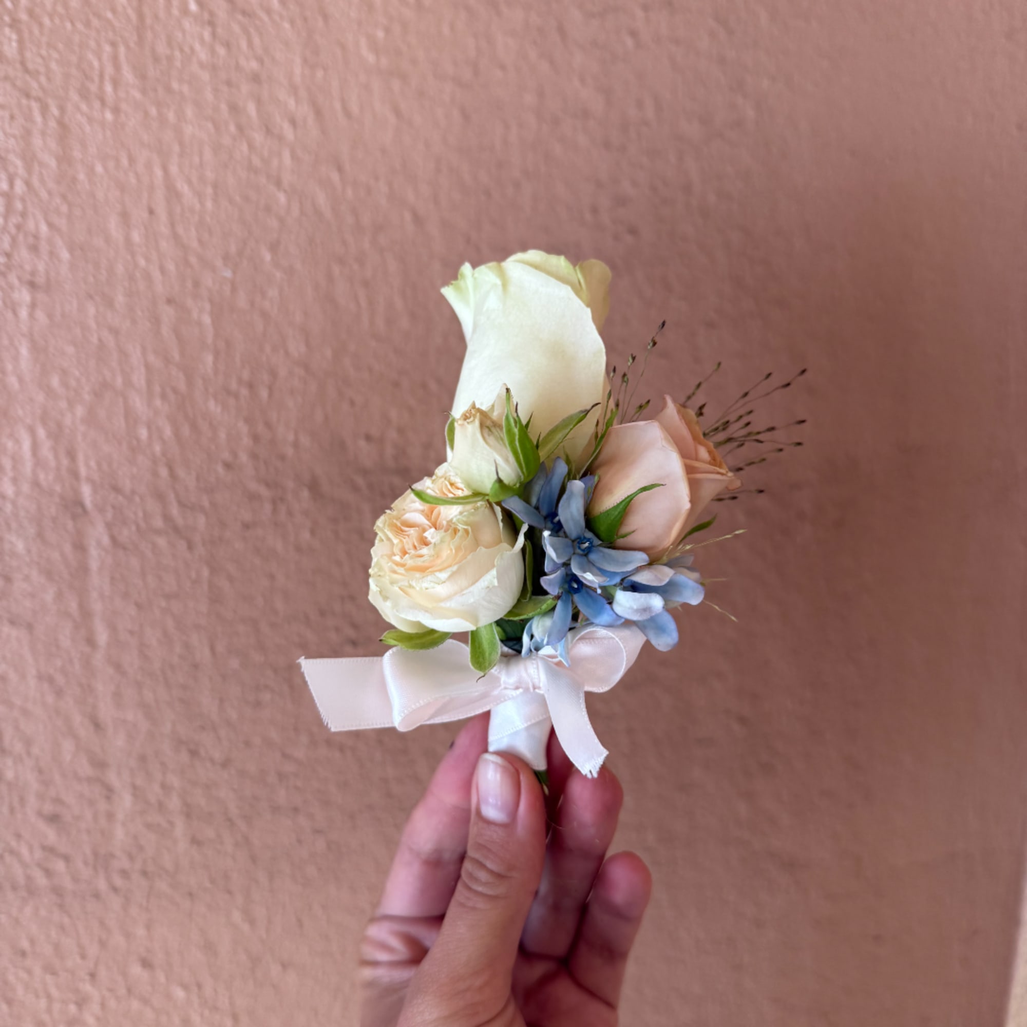 Small wedding boutonniere with cream and blush roses and blue flowers tied with a white ribbon