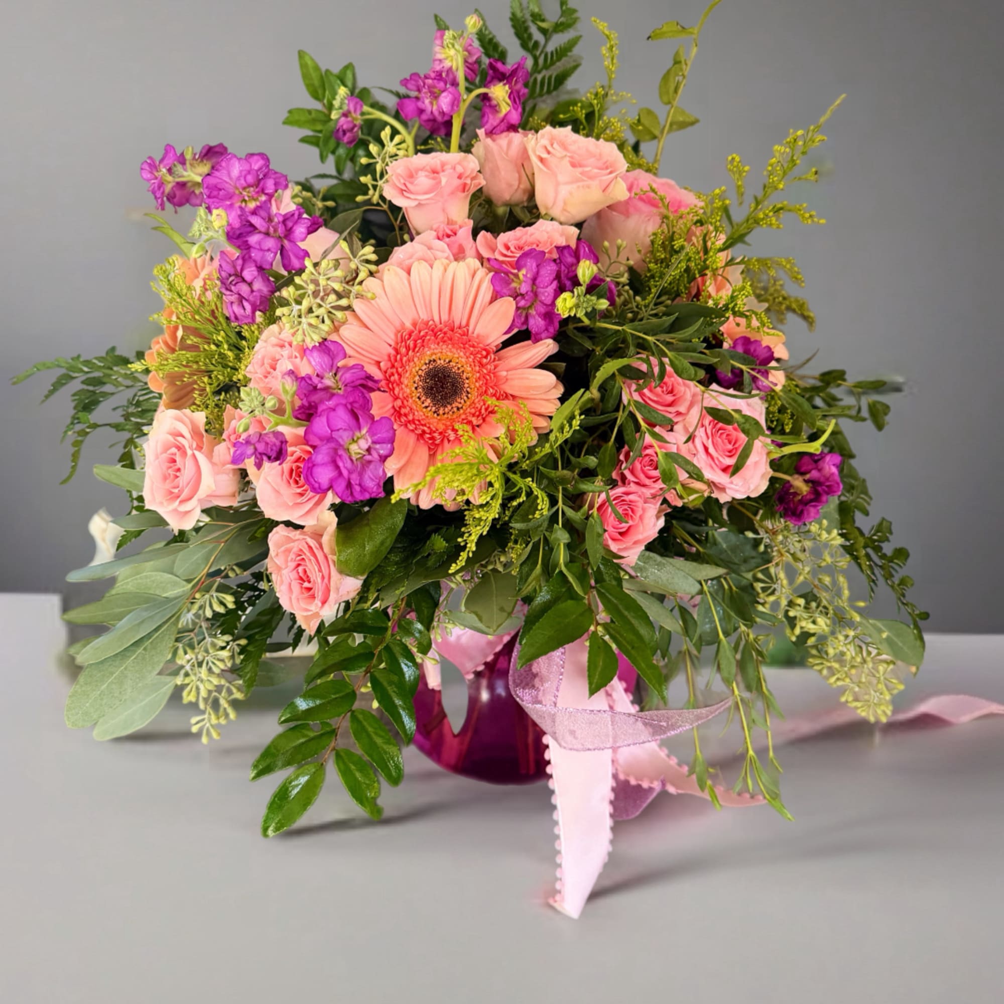 Pink roses and a peach gerbera daisy in a purple vase