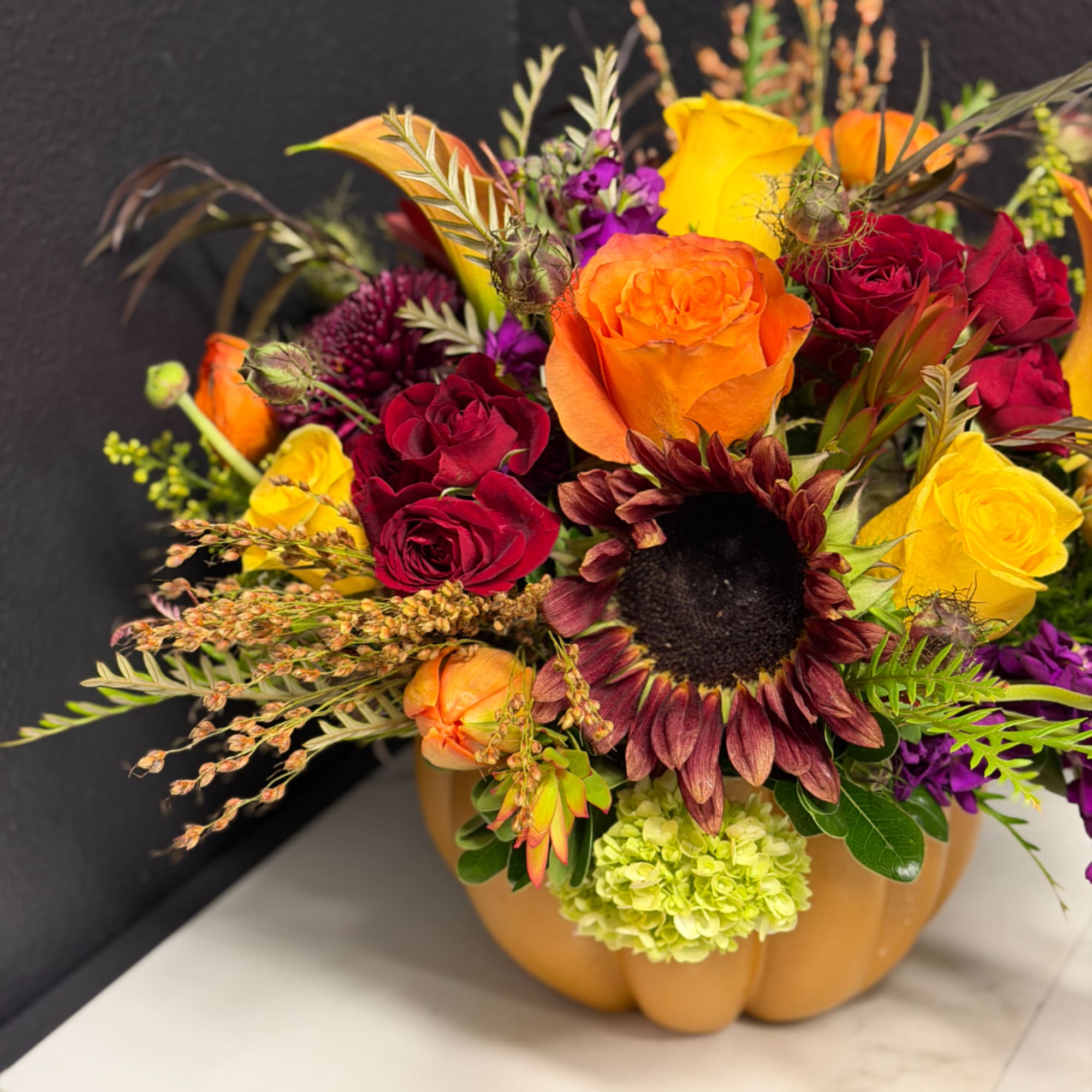 Mixed bouquet in a pumpkin-shaped container with roses and a sunflower