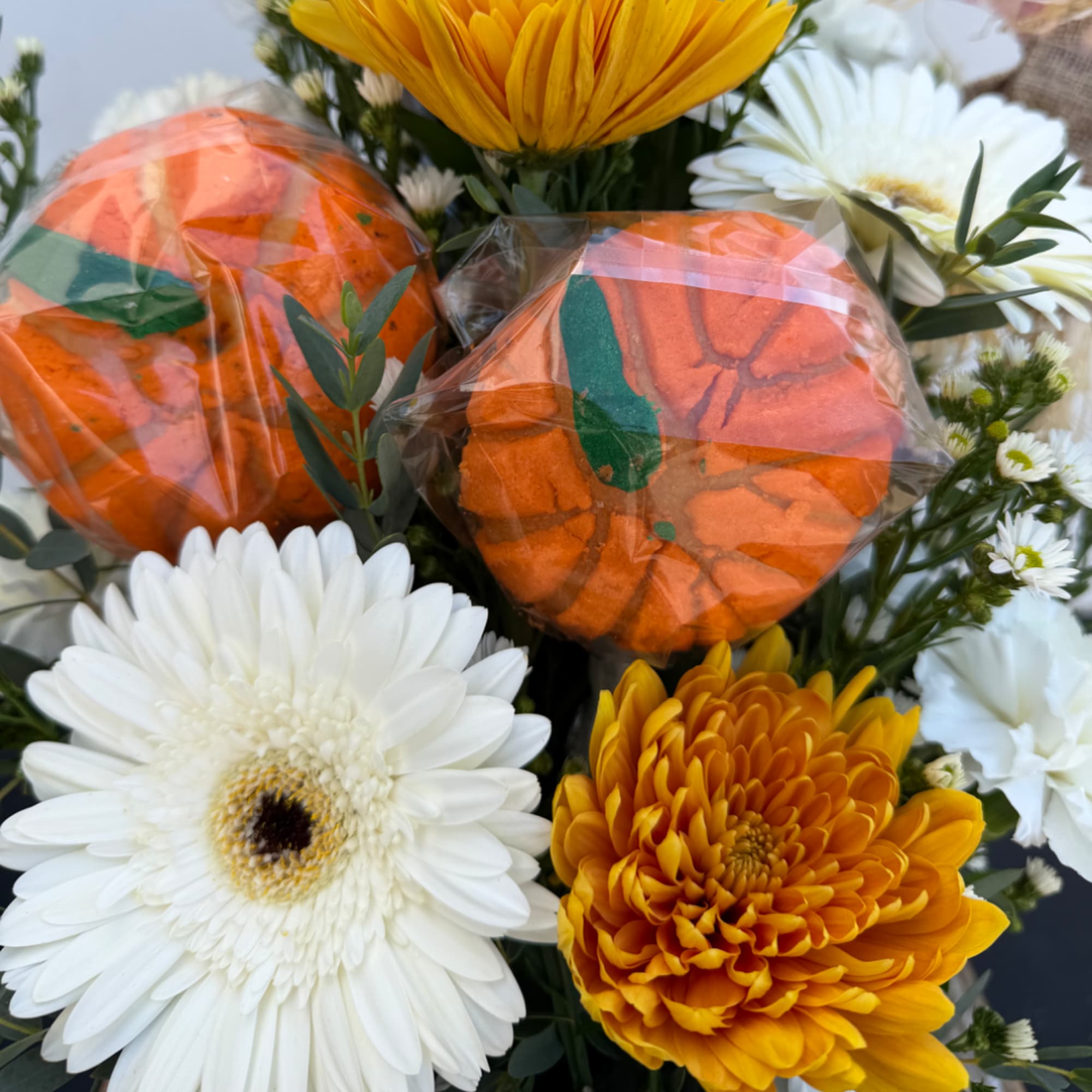 Orange pumpkin-shaped treats among white and yellow flowers