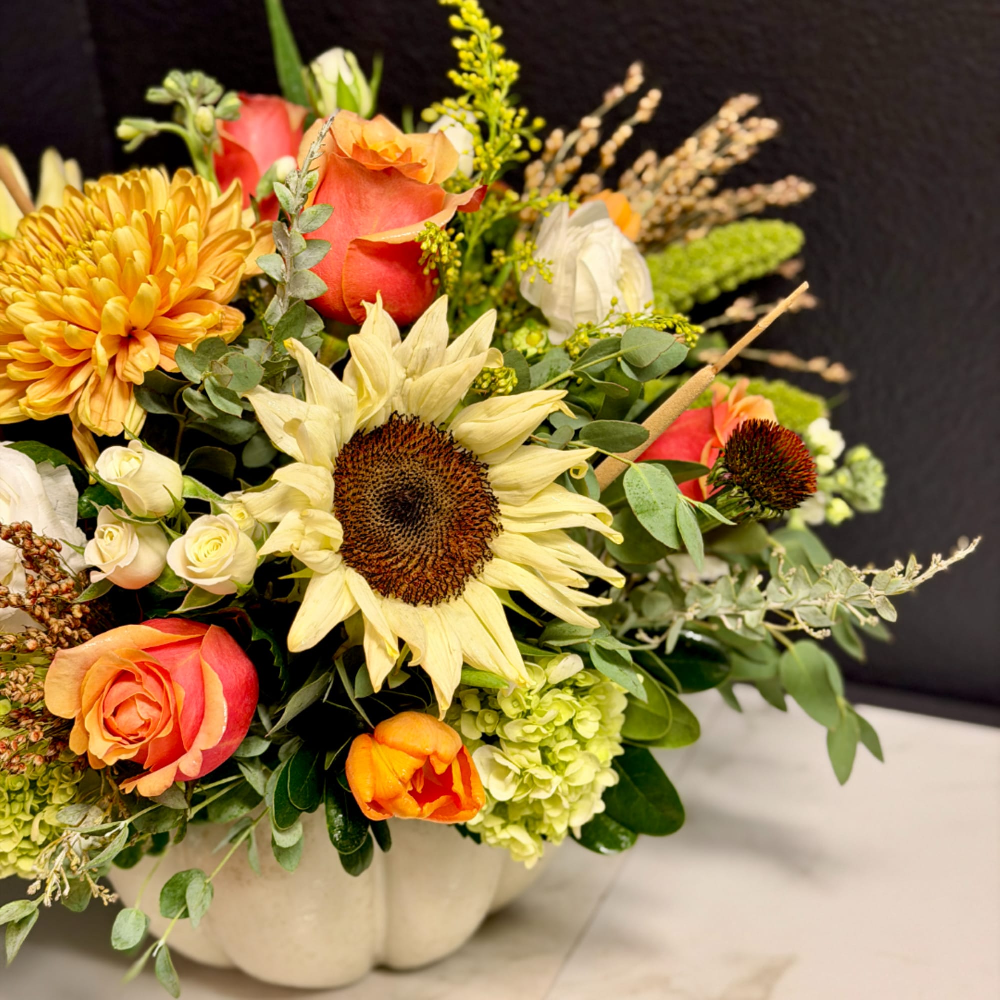 Mixed bouquet with sunflowers, roses, and chrysanthemums in a white pumpkin vase