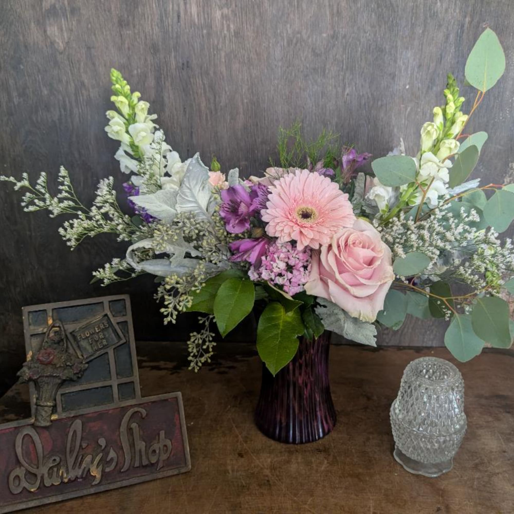 Pink and purple mixed bouquet in a dark vase with decorative accents nearby
