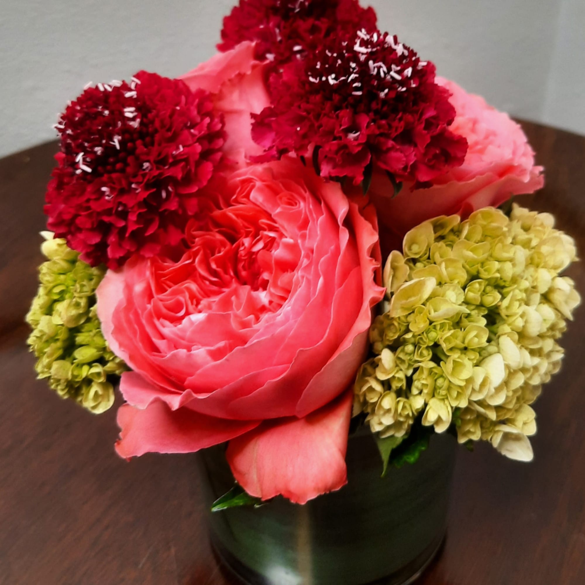 Pink rose arrangement with red carnations in a dark vase