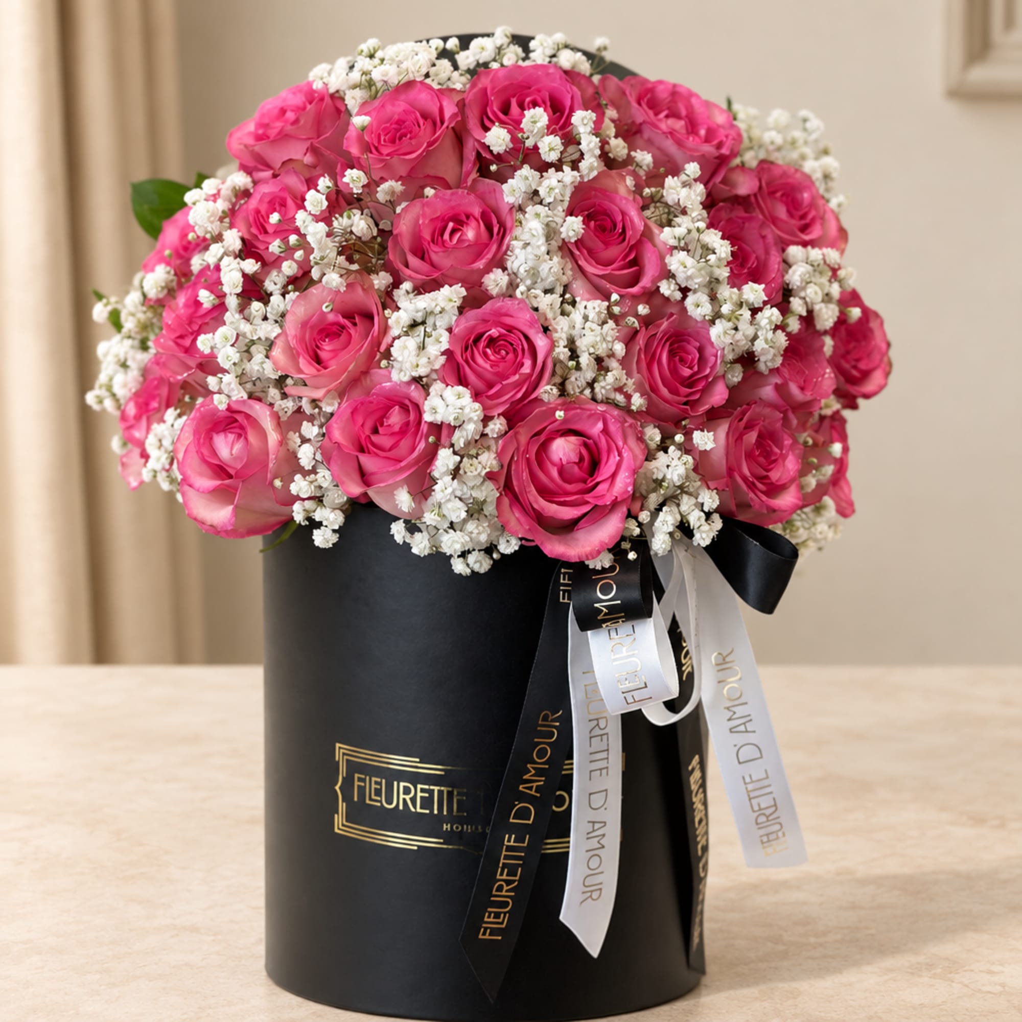 Pink roses and white baby's breath in a black hatbox with ribbons