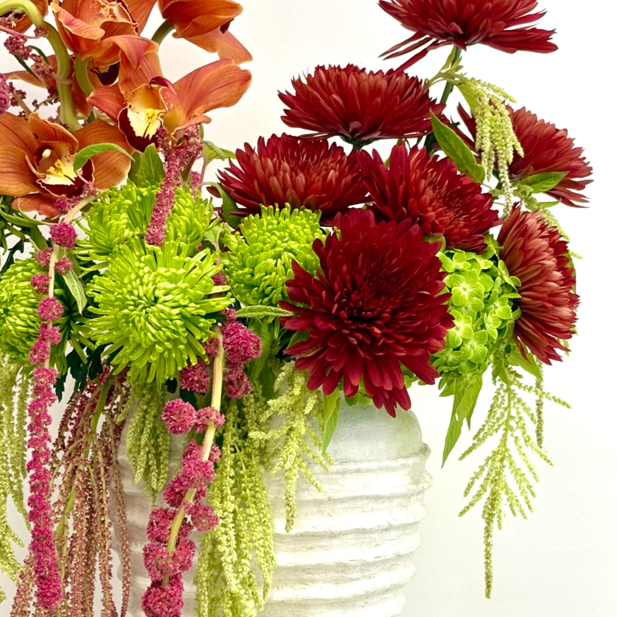 Mixed bouquet with red chrysanthemums, green blooms, and orange orchids in a white vase