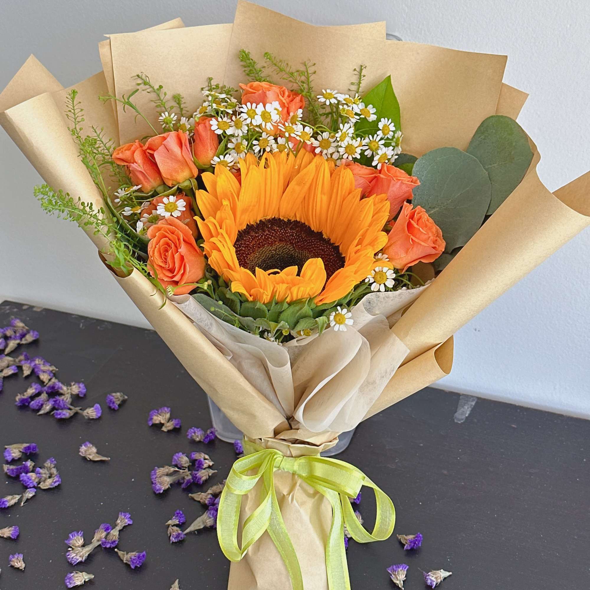Bouquet with a sunflower, orange roses, and small white daisies in kraft paper