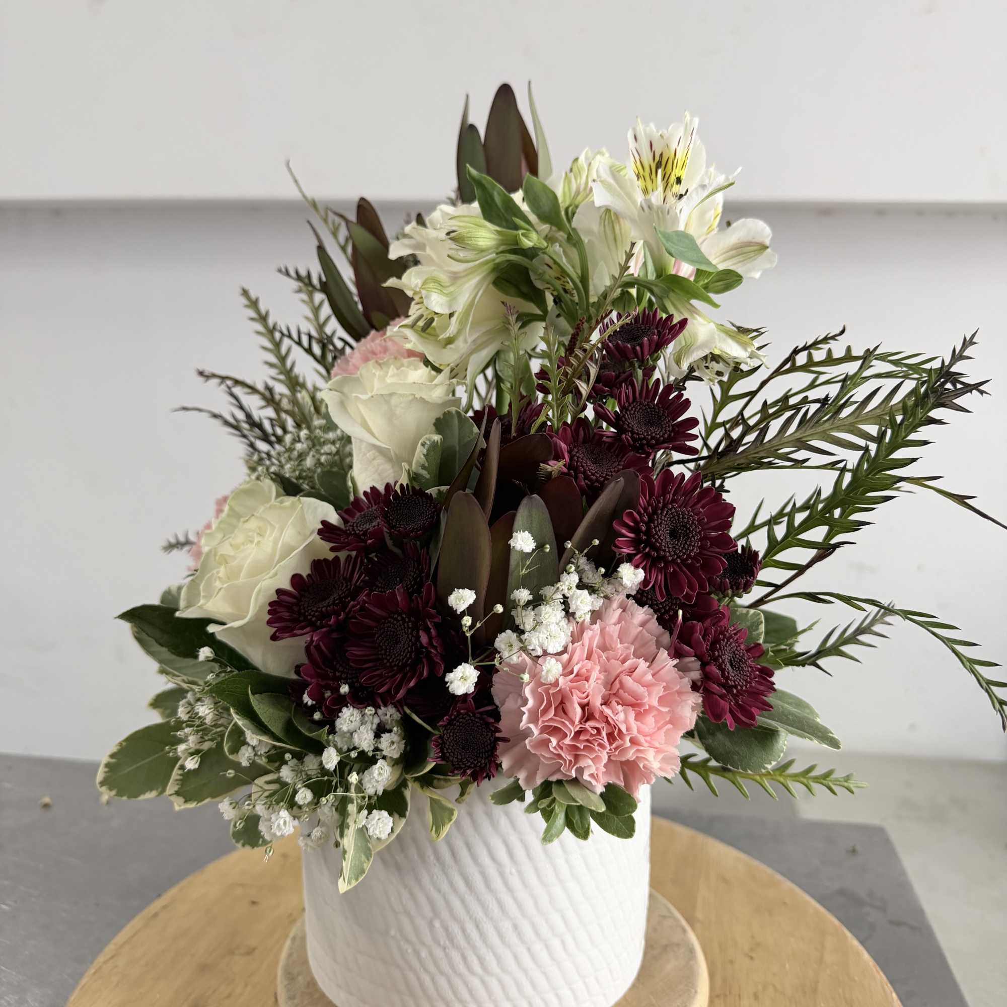 Mixed bouquet in a white textured vase with pink, white, and burgundy flowers