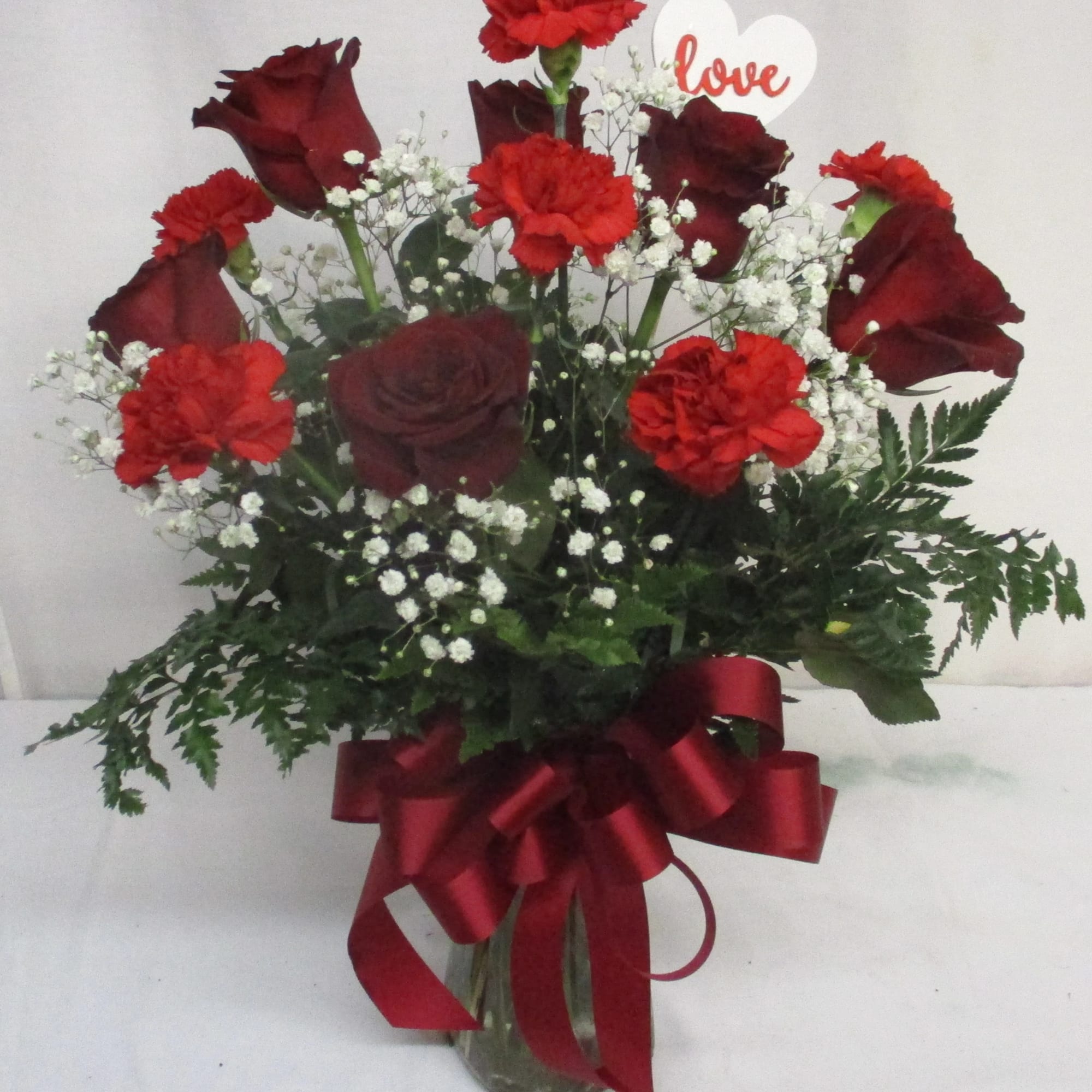 Red roses and carnations in a glass vase with a heart "love" pick