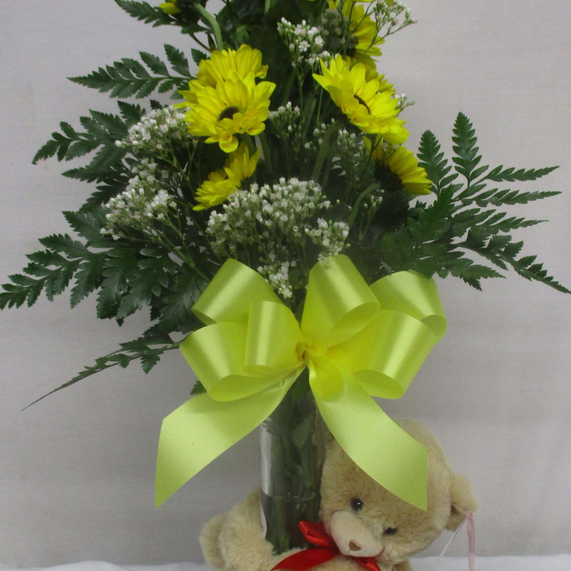 Yellow daisy bouquet in a glass vase with a teddy bear at the base