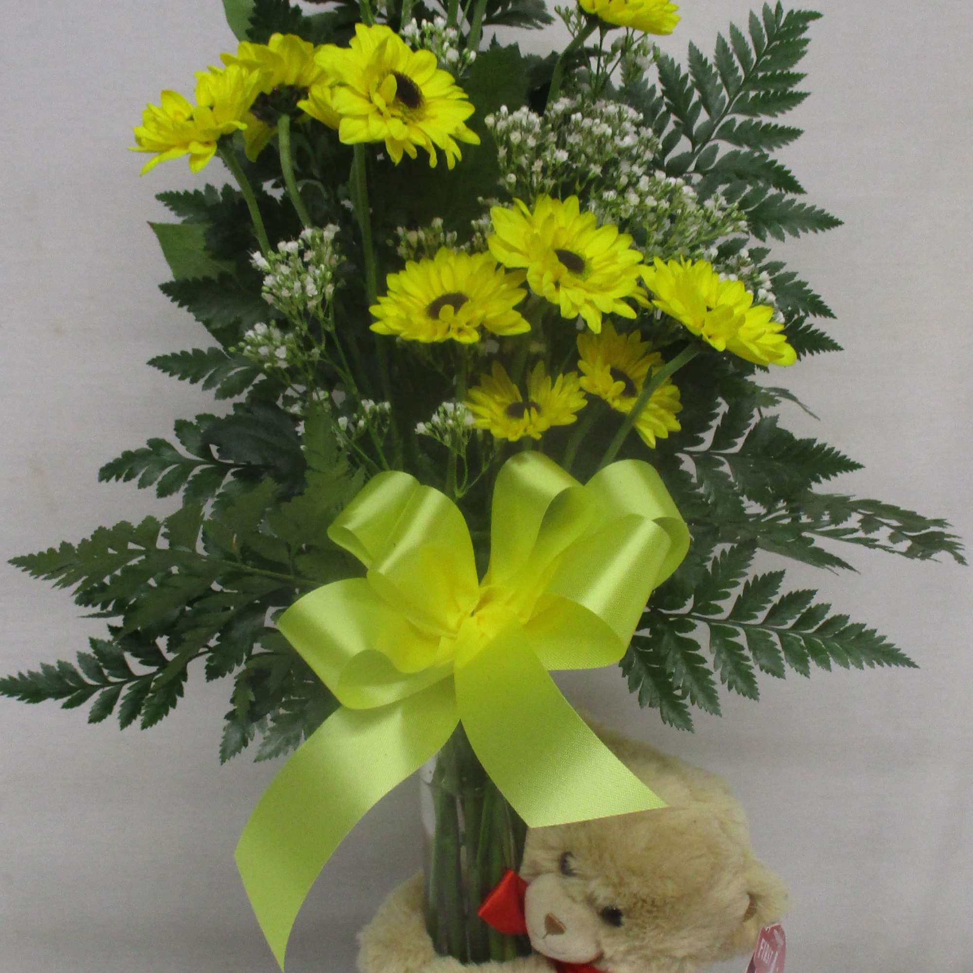 Yellow daisy bouquet in a glass vase with a teddy bear