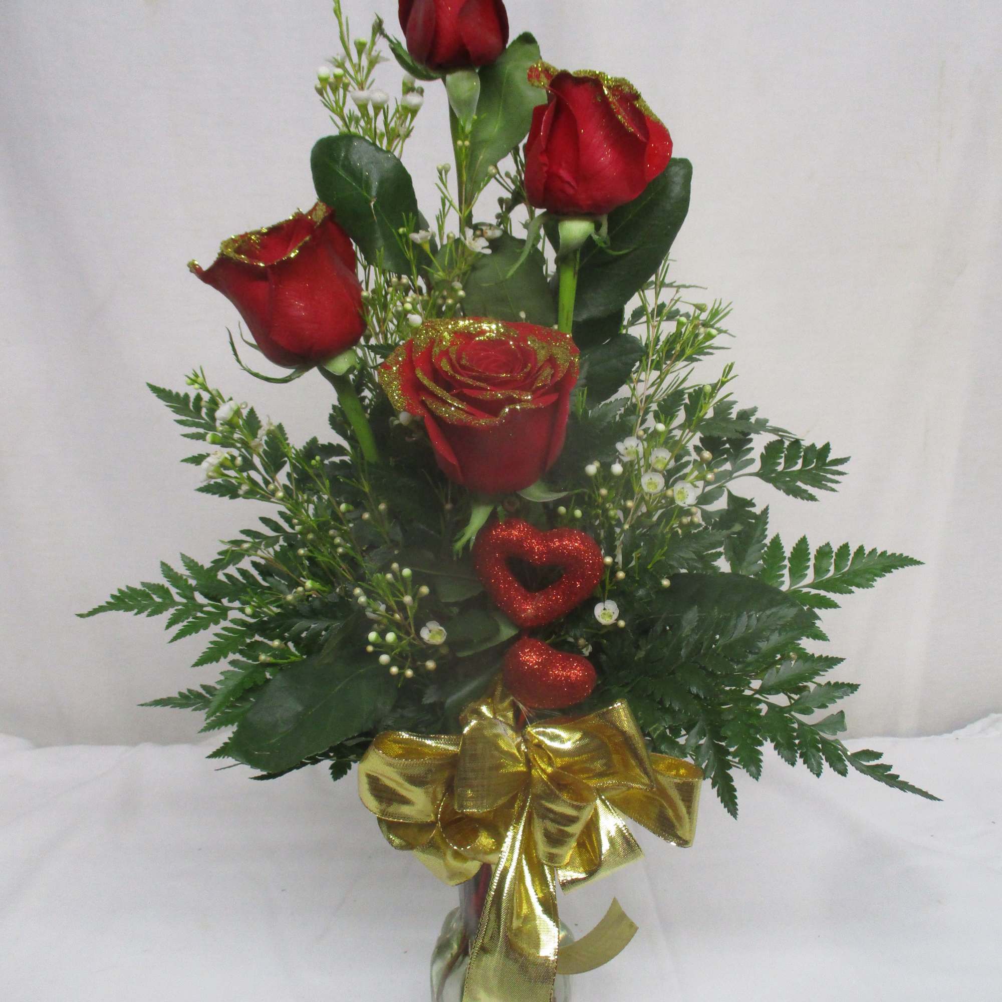 Red roses in a glass vase with a gold bow and glittery heart accents