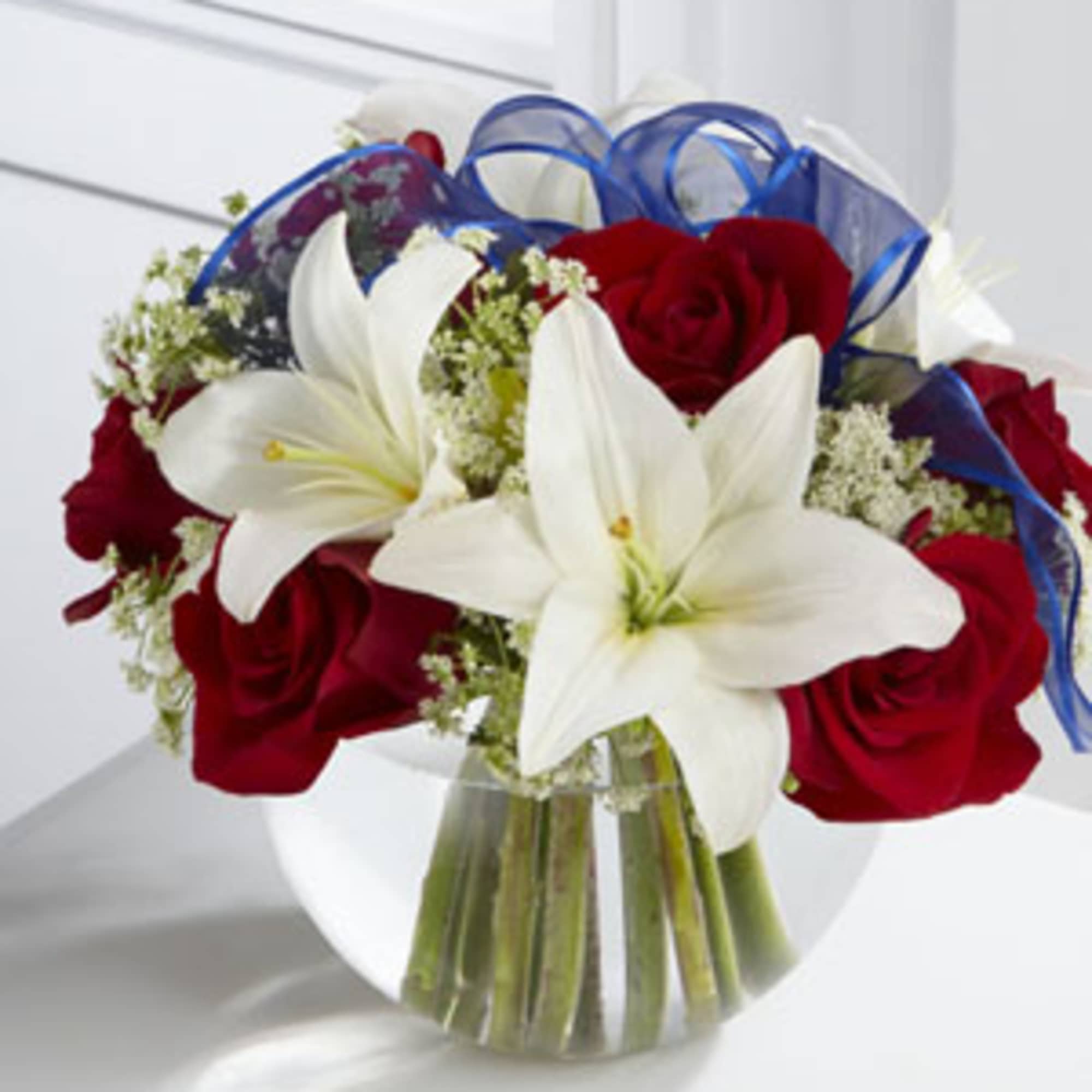 Red roses and white lilies in a clear glass vase with blue ribbon