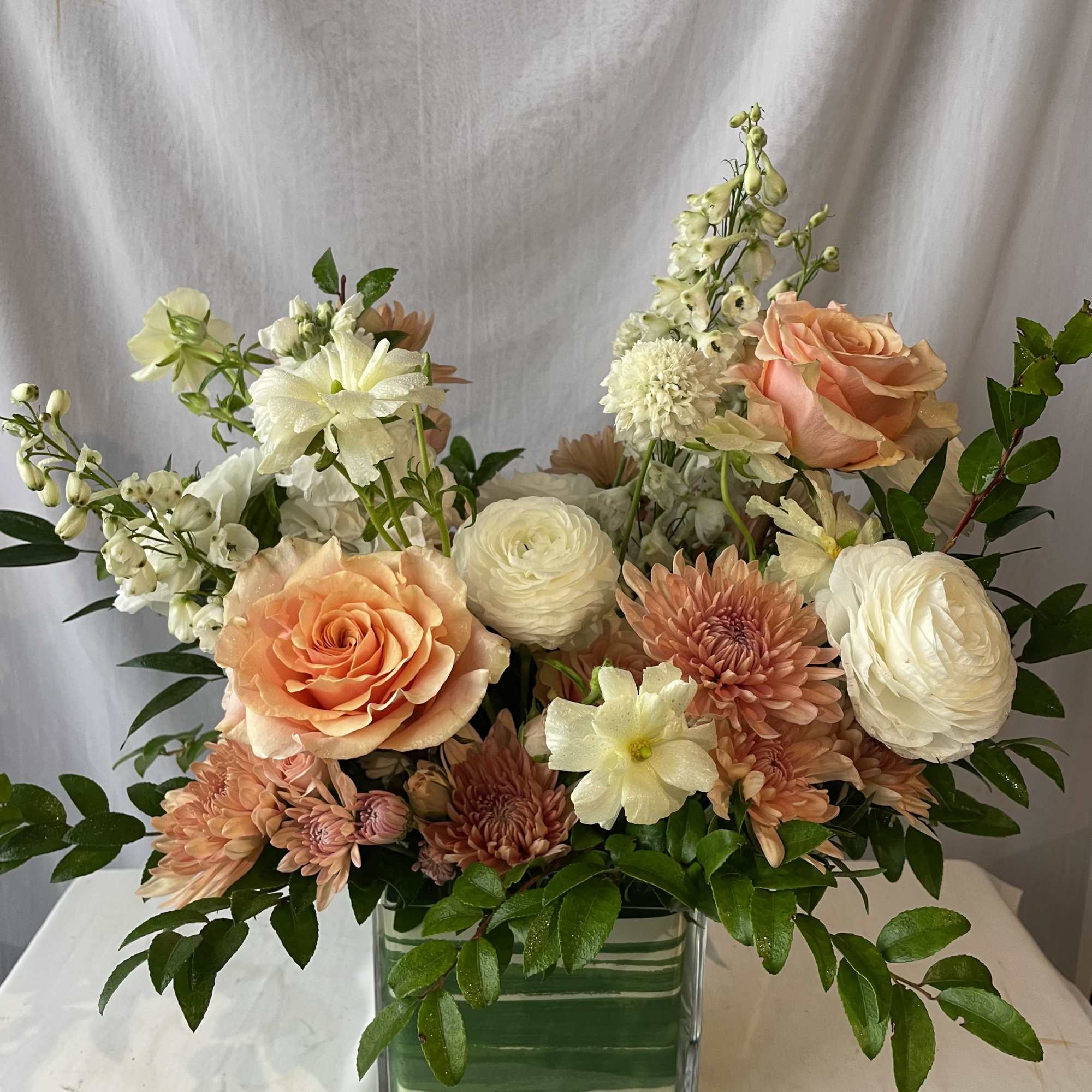 Peach and white mixed flower arrangement in a square glass vase