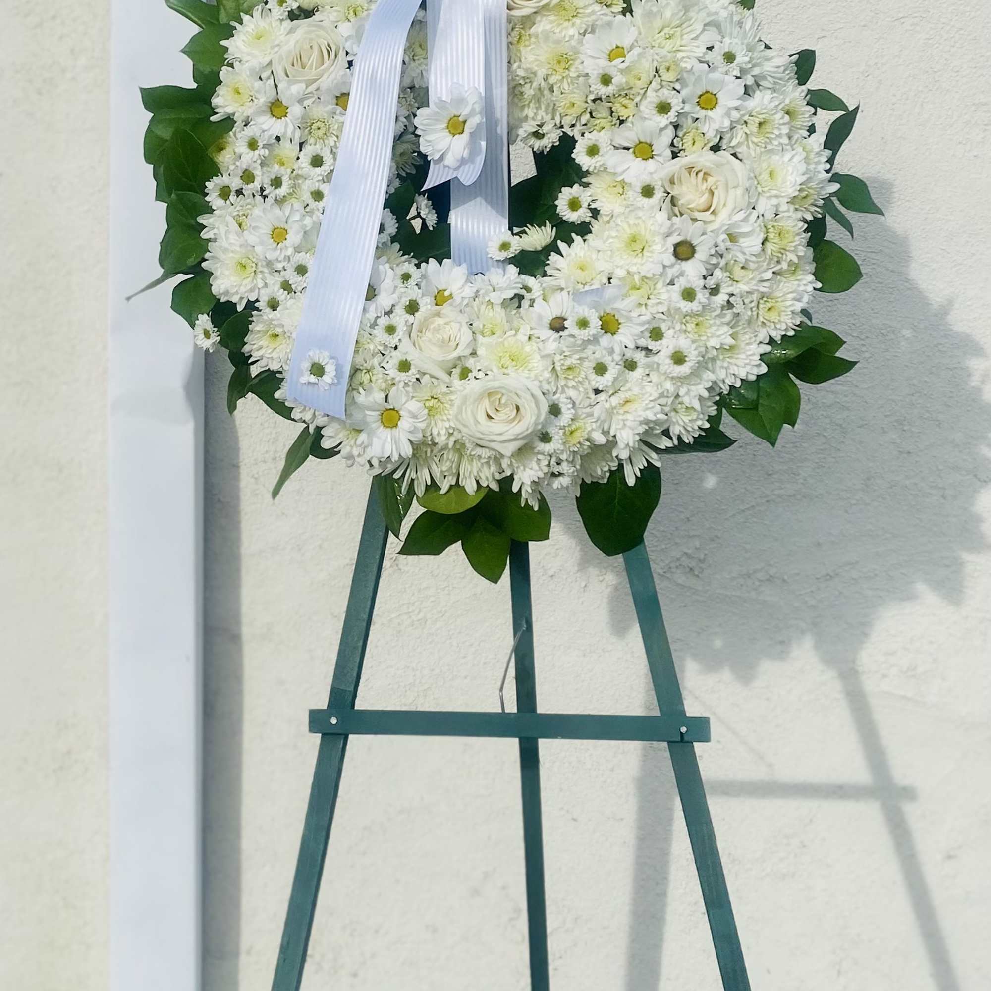 White floral wreath on a standing easel with a large white bow