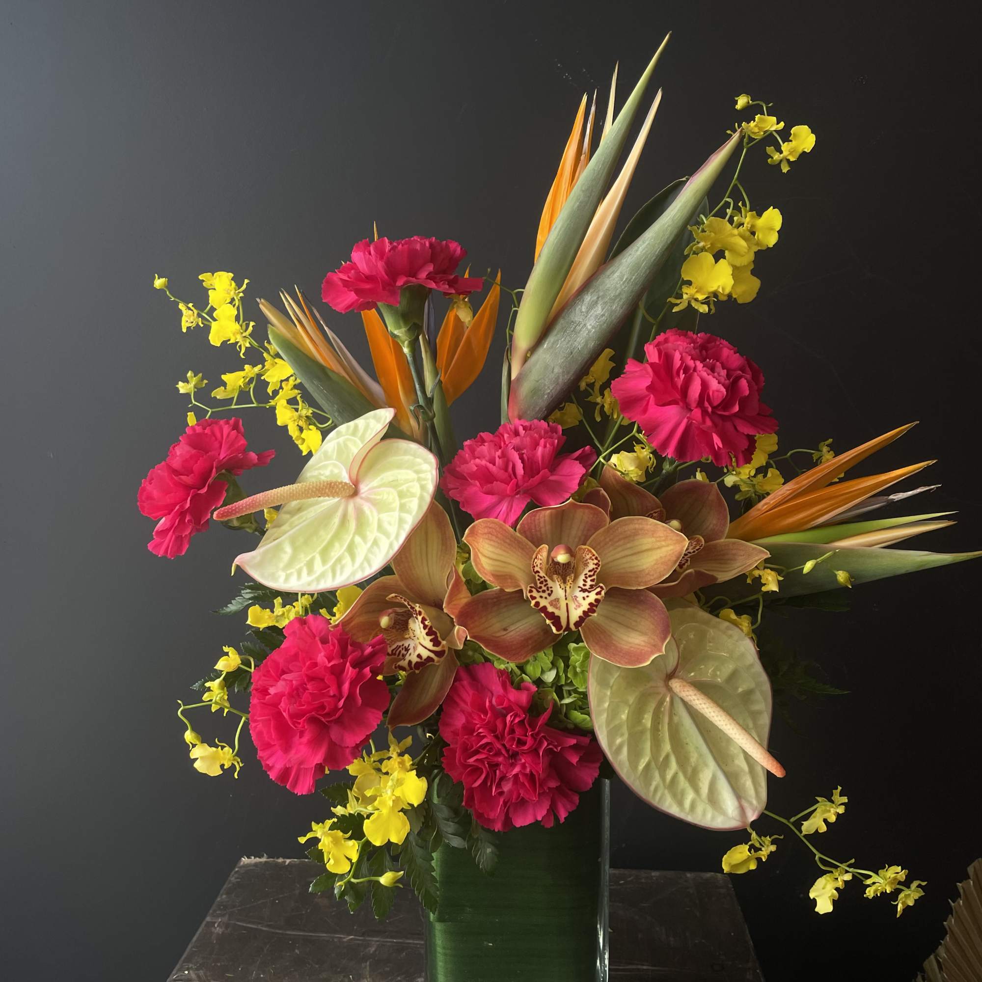 Tropical bouquet with pink carnations, orchids, and anthuriums in a glass vase