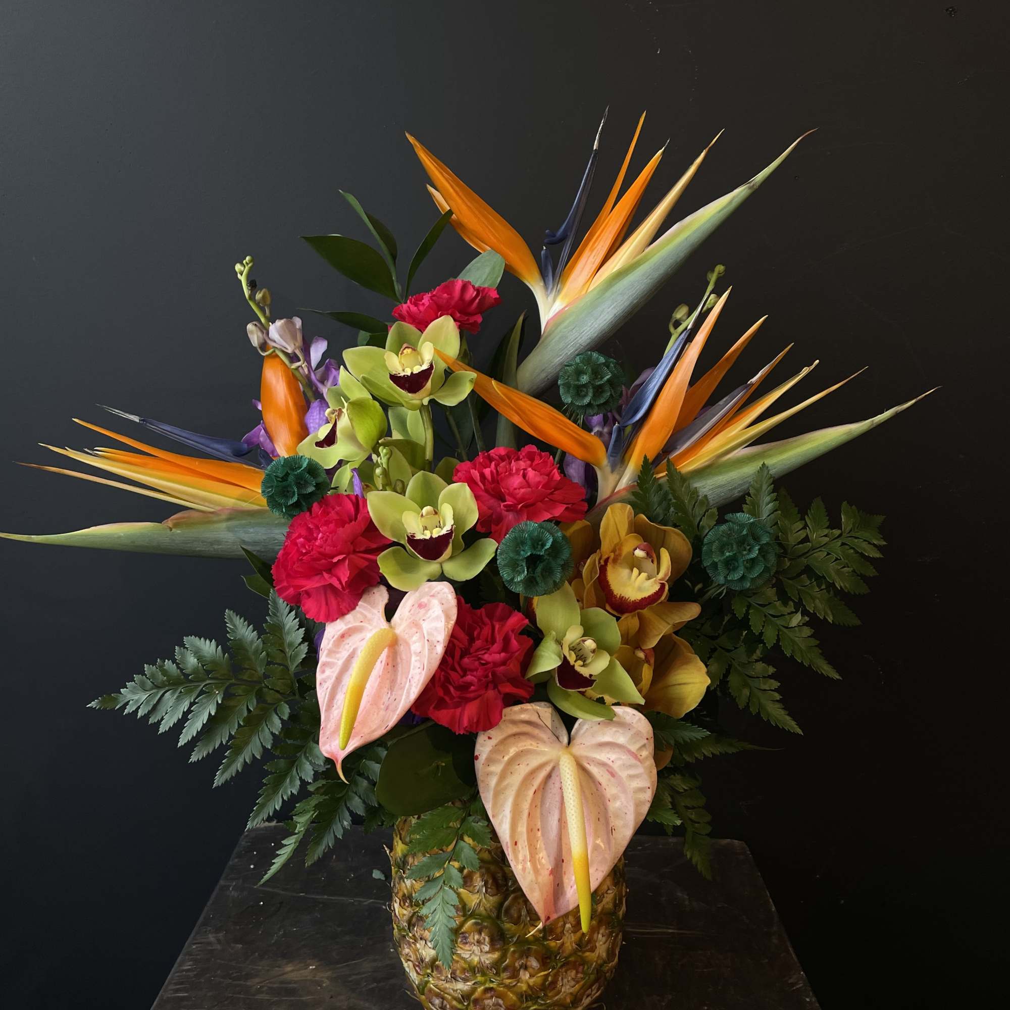 Tropical flower arrangement in a pineapple container with orchids and anthuriums