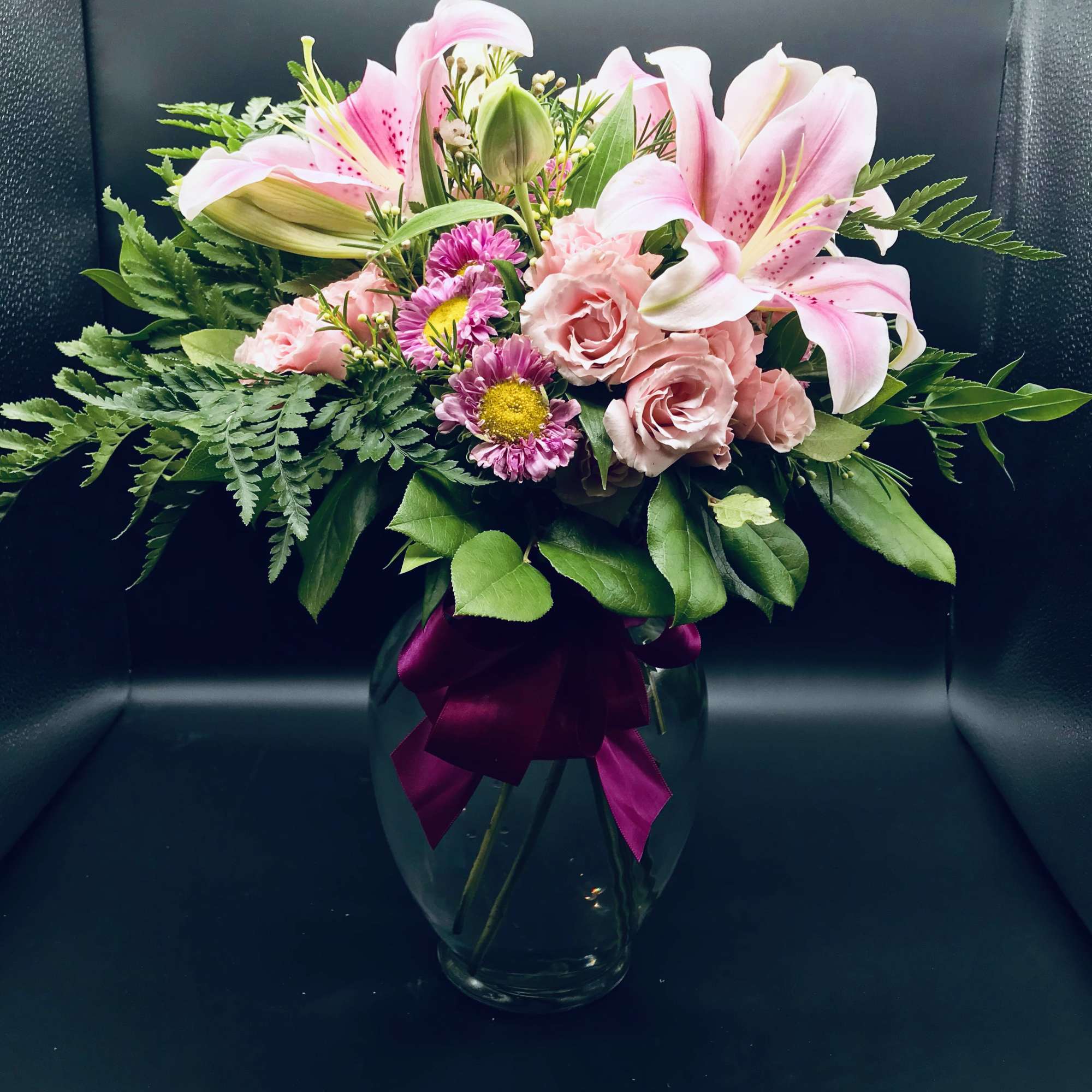 Pink lilies and roses in a glass vase with a magenta ribbon
