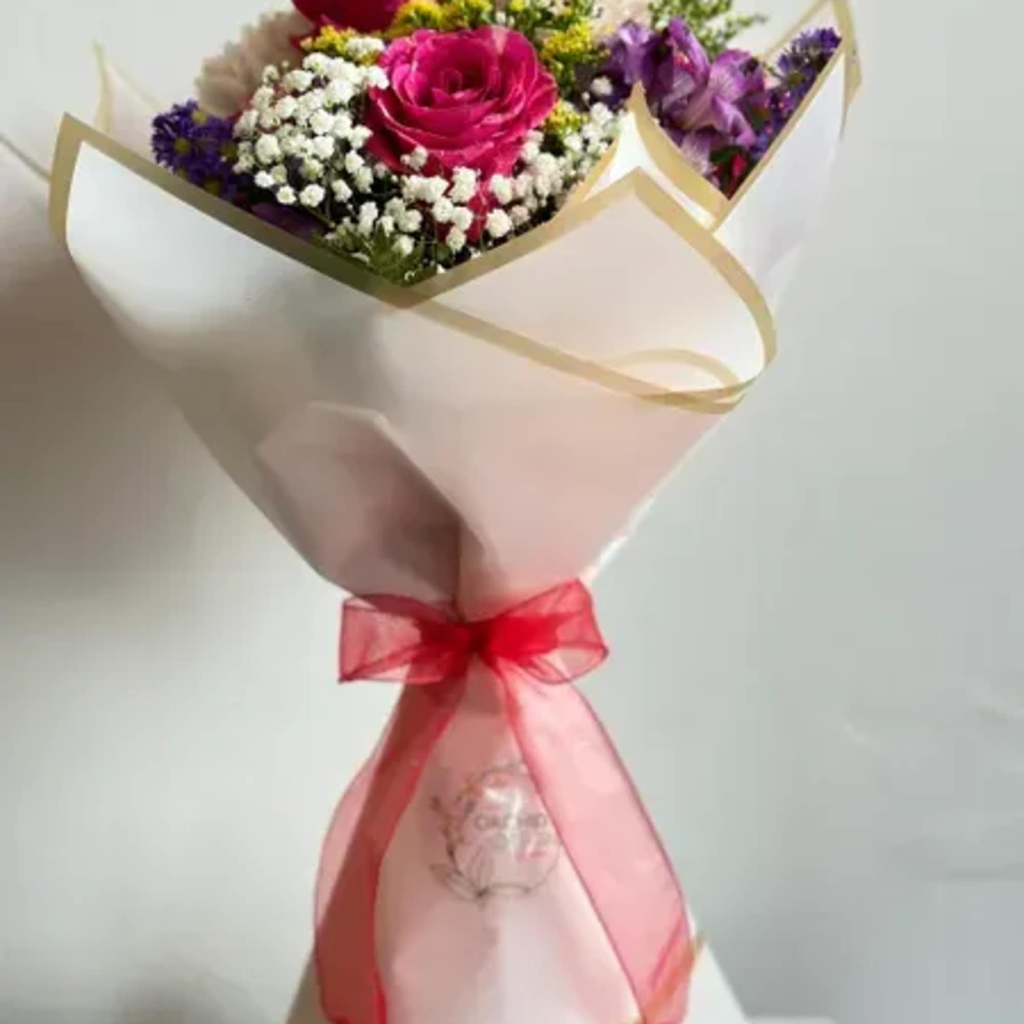 Bouquet of pink roses, purple flowers, and white filler wrapped in paper with a red ribbon
