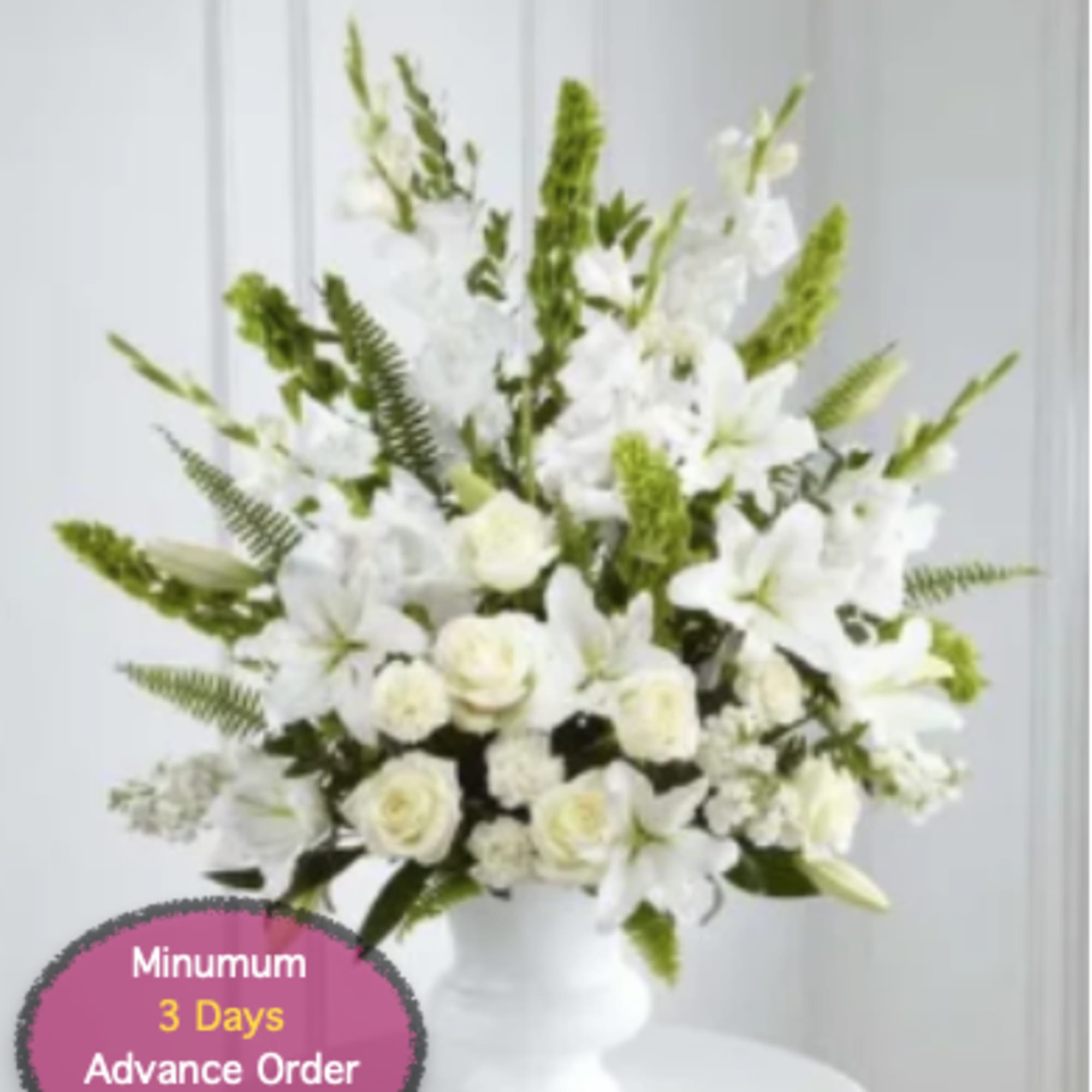 White floral arrangement in a white pedestal vase with tall green accents