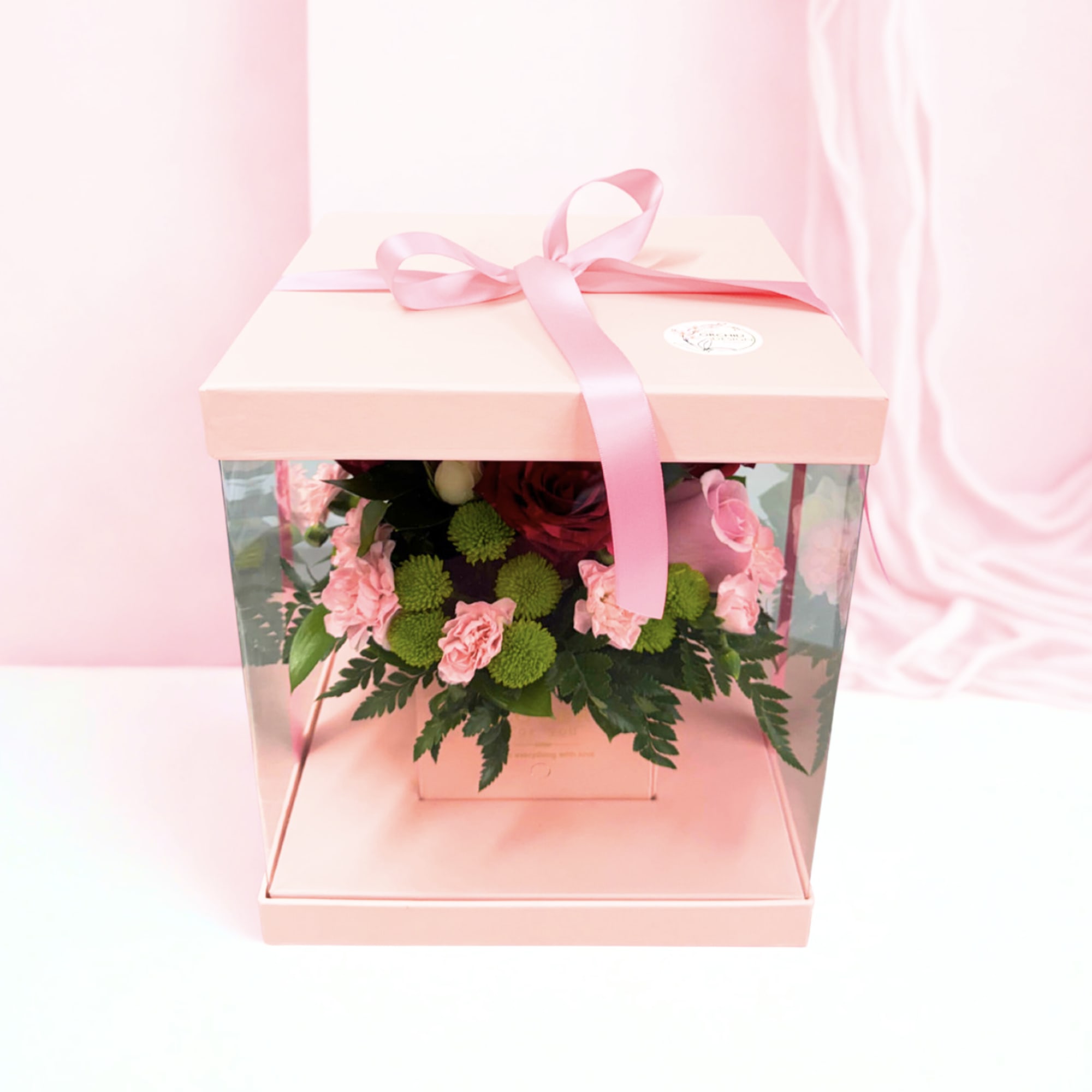 Pink gift box with a ribbon and a small floral arrangement inside