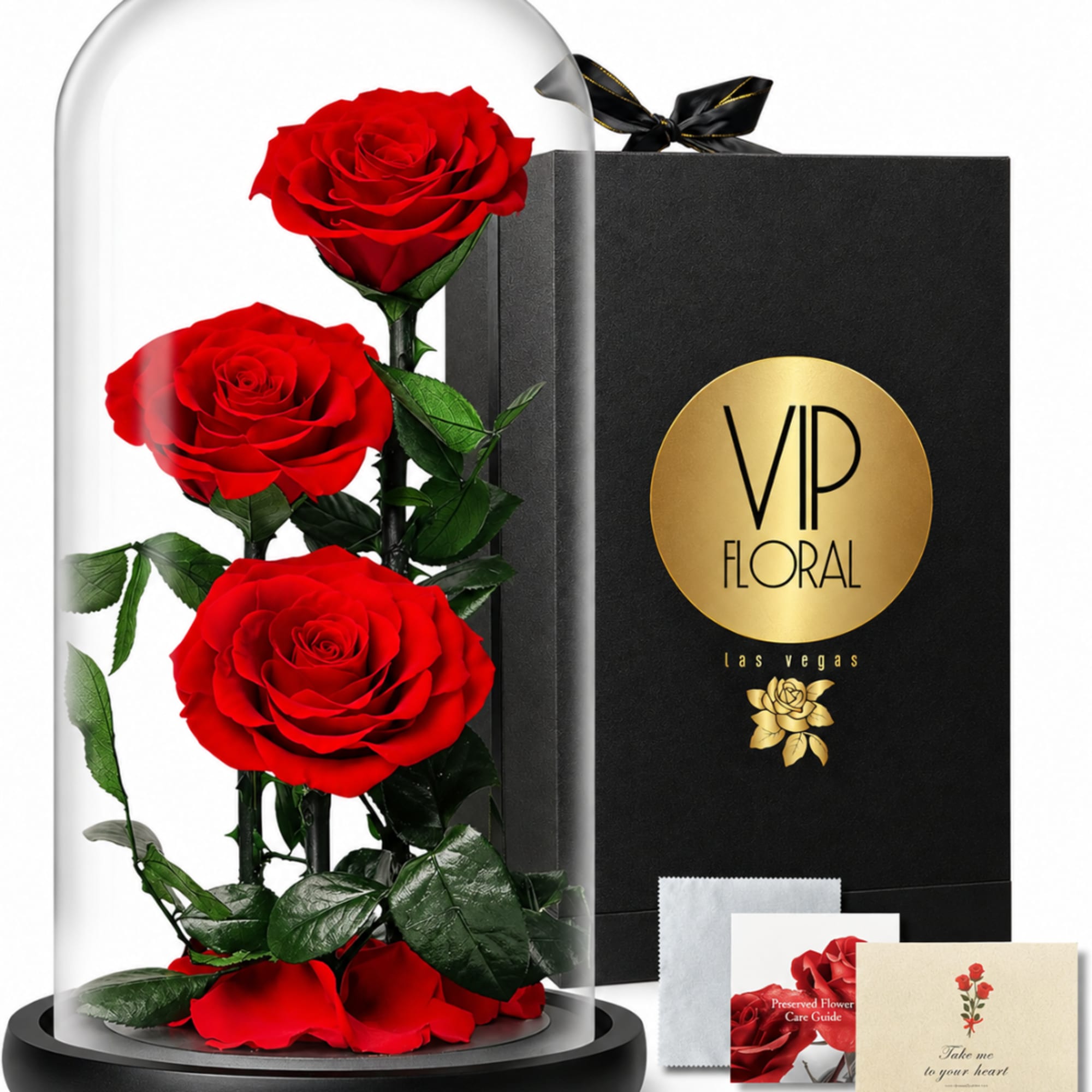 Three red roses under a glass dome beside a black gift box