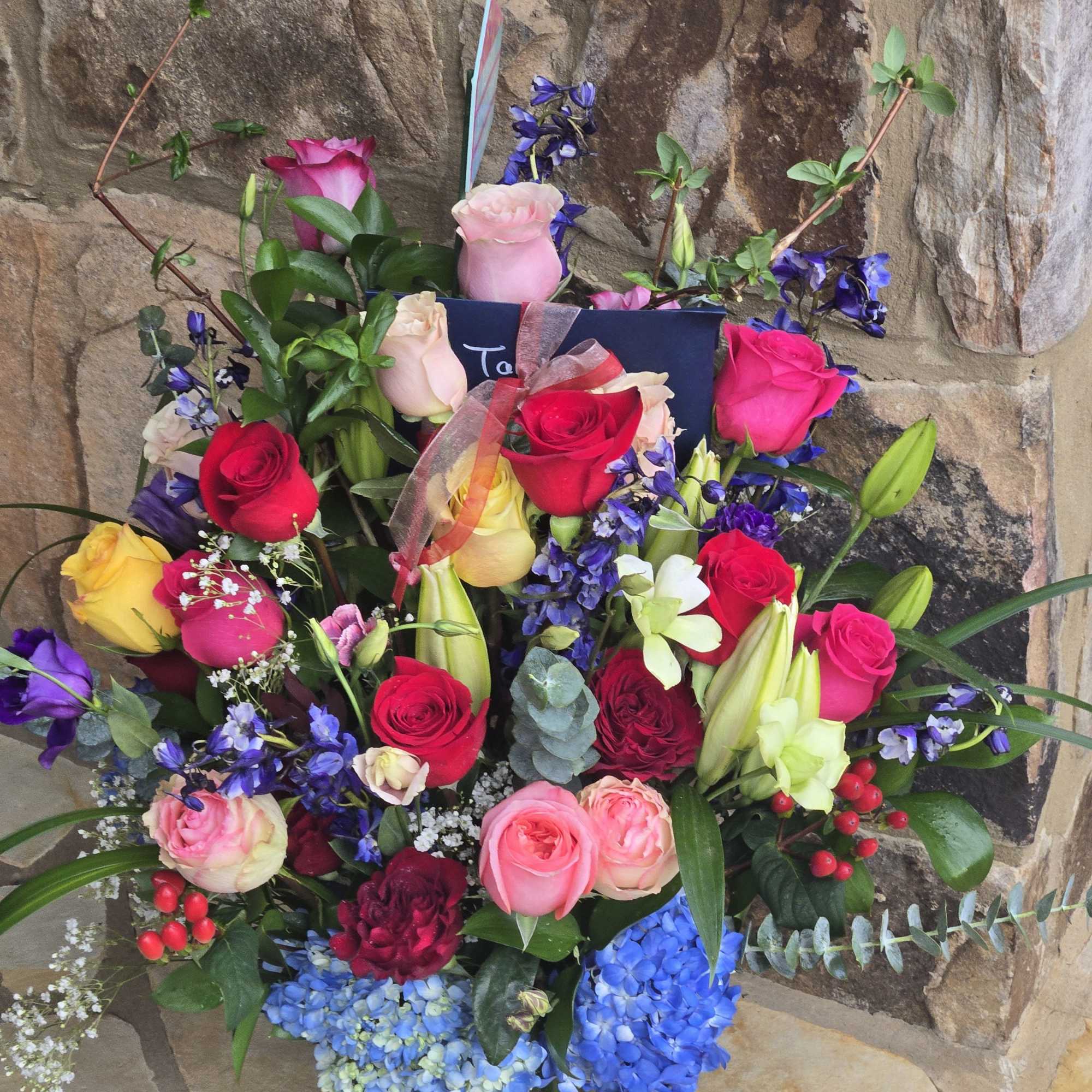 Tall mixed bouquet of roses, lilies, hydrangeas, and accent blooms in a clear glass vase