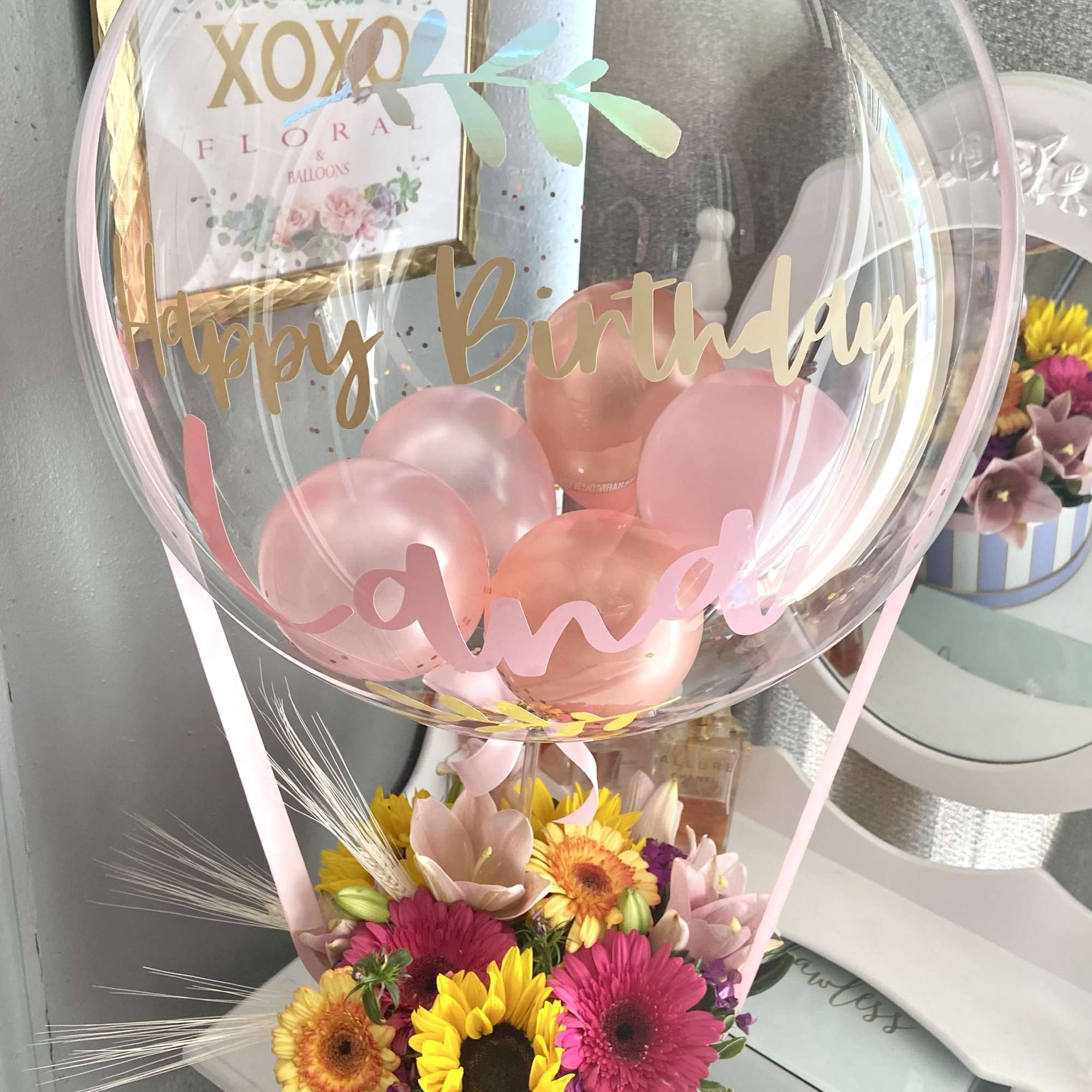 Birthday balloon arrangement with pink balloons and mixed flowers in a striped box