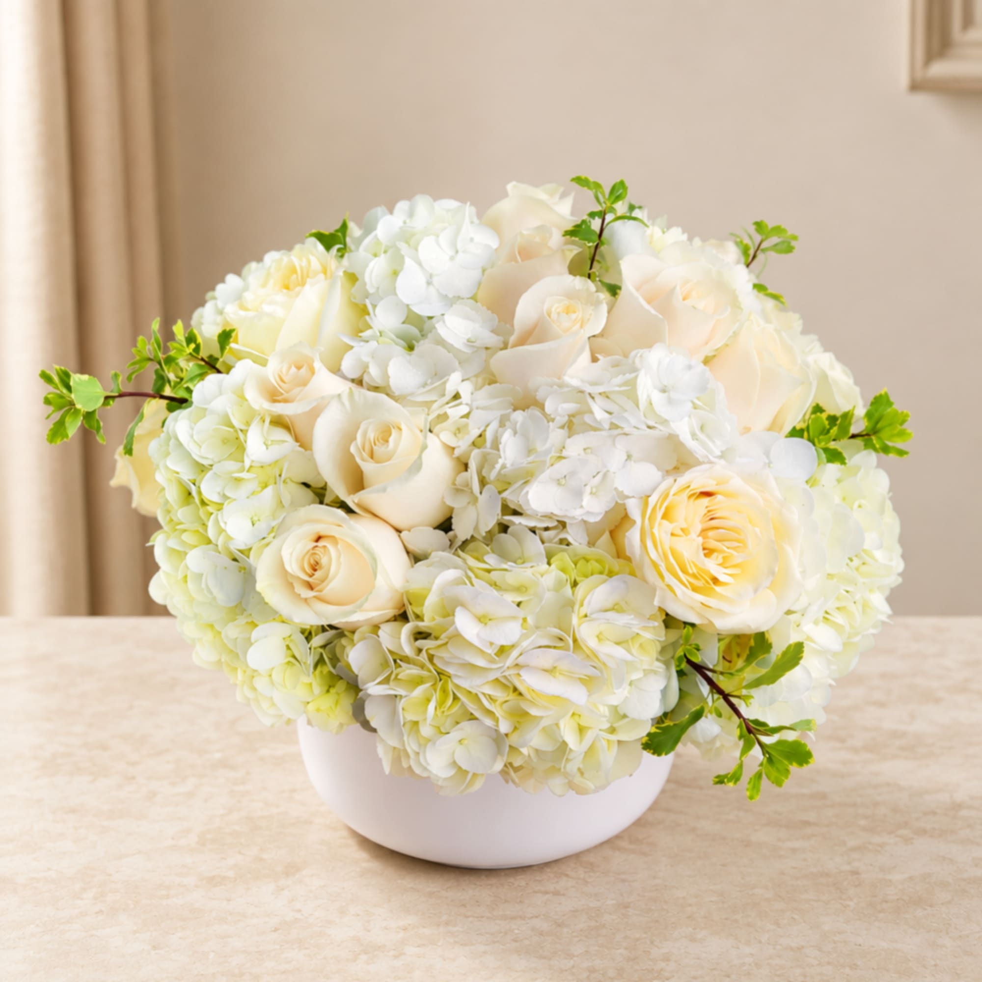 Cream roses and white hydrangeas arranged in a white bowl vase