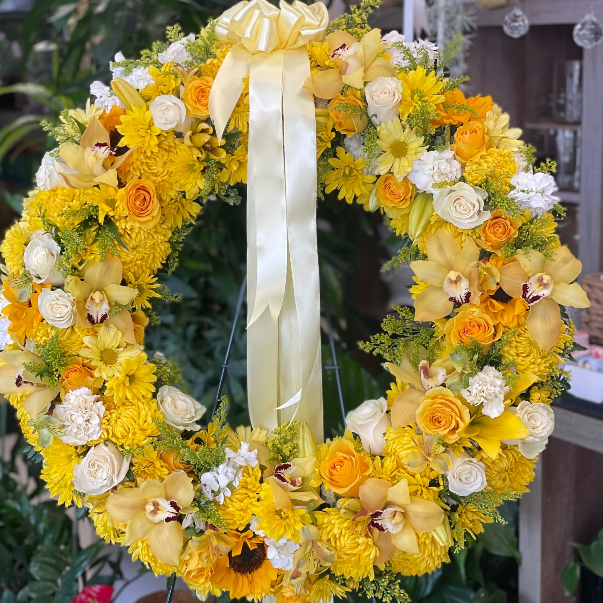Standing wreath of yellow and white flowers with a pale yellow ribbon bow.