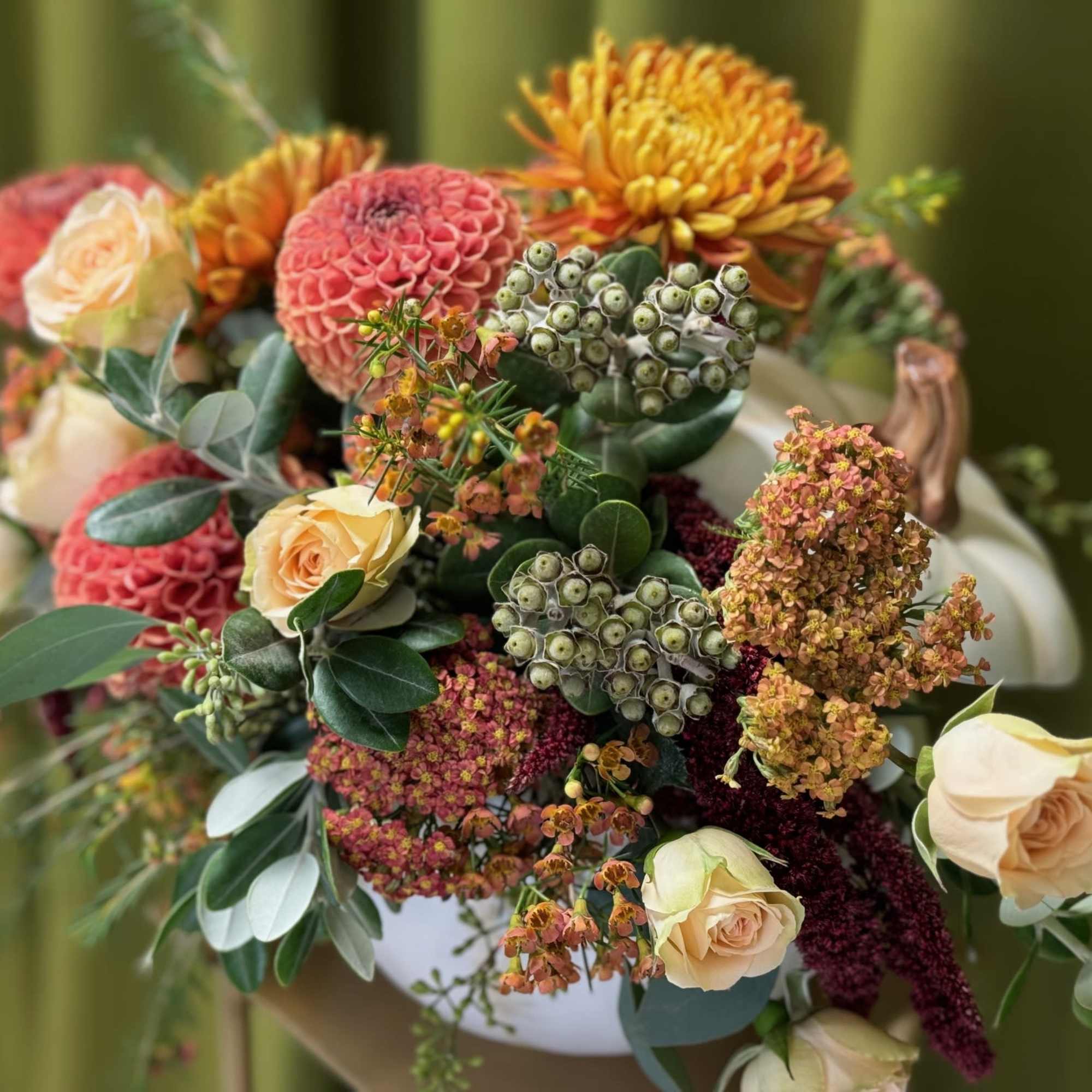 Mixed bouquet of peach roses and orange blooms in a white vase