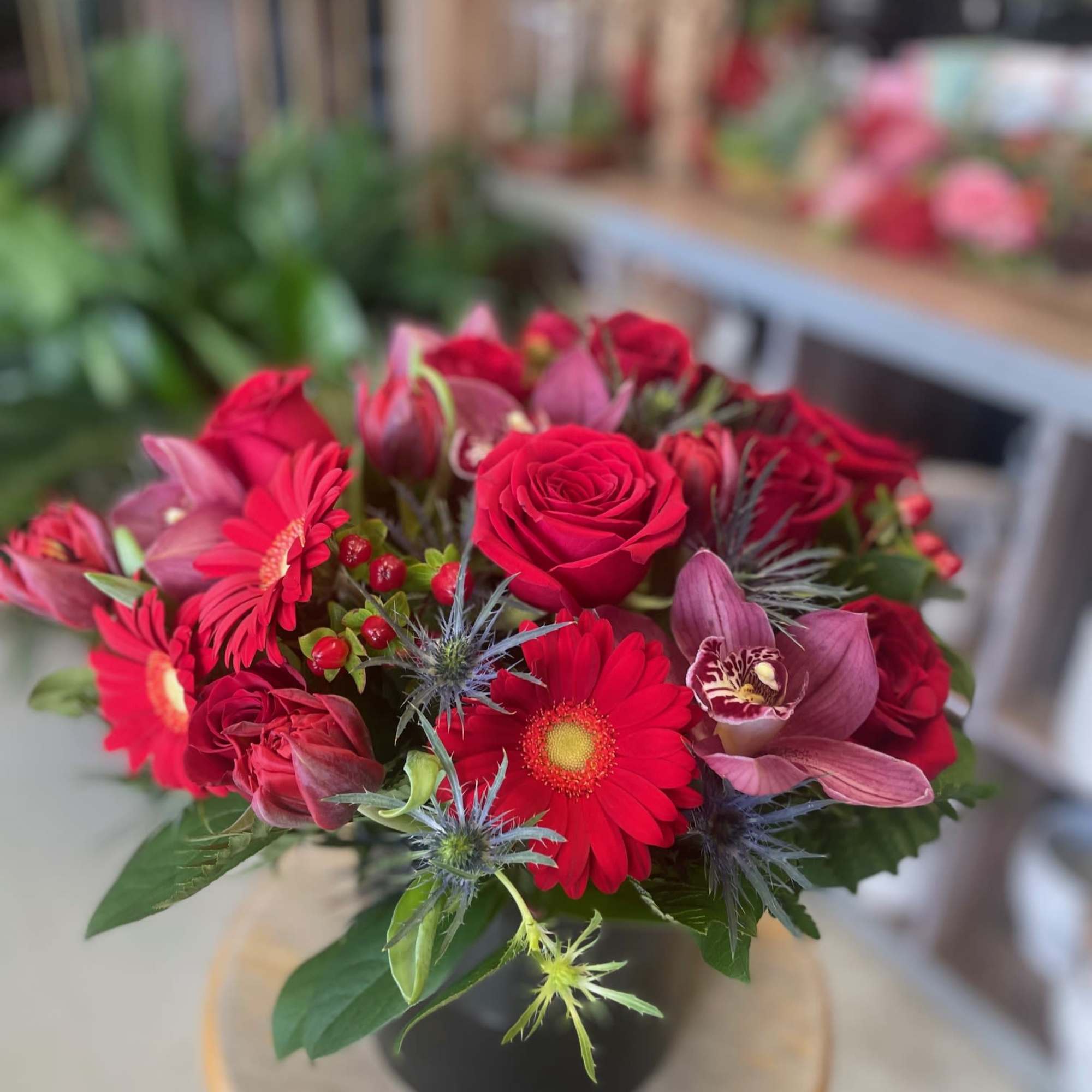 Low arrangement of red roses, gerbera daisies, and mauve orchids in a black vase.