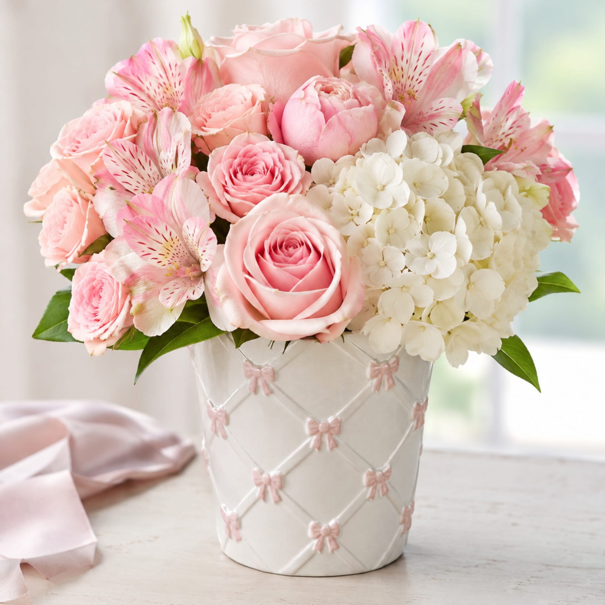 Pink roses and alstroemeria arranged in a white vase with pink bows