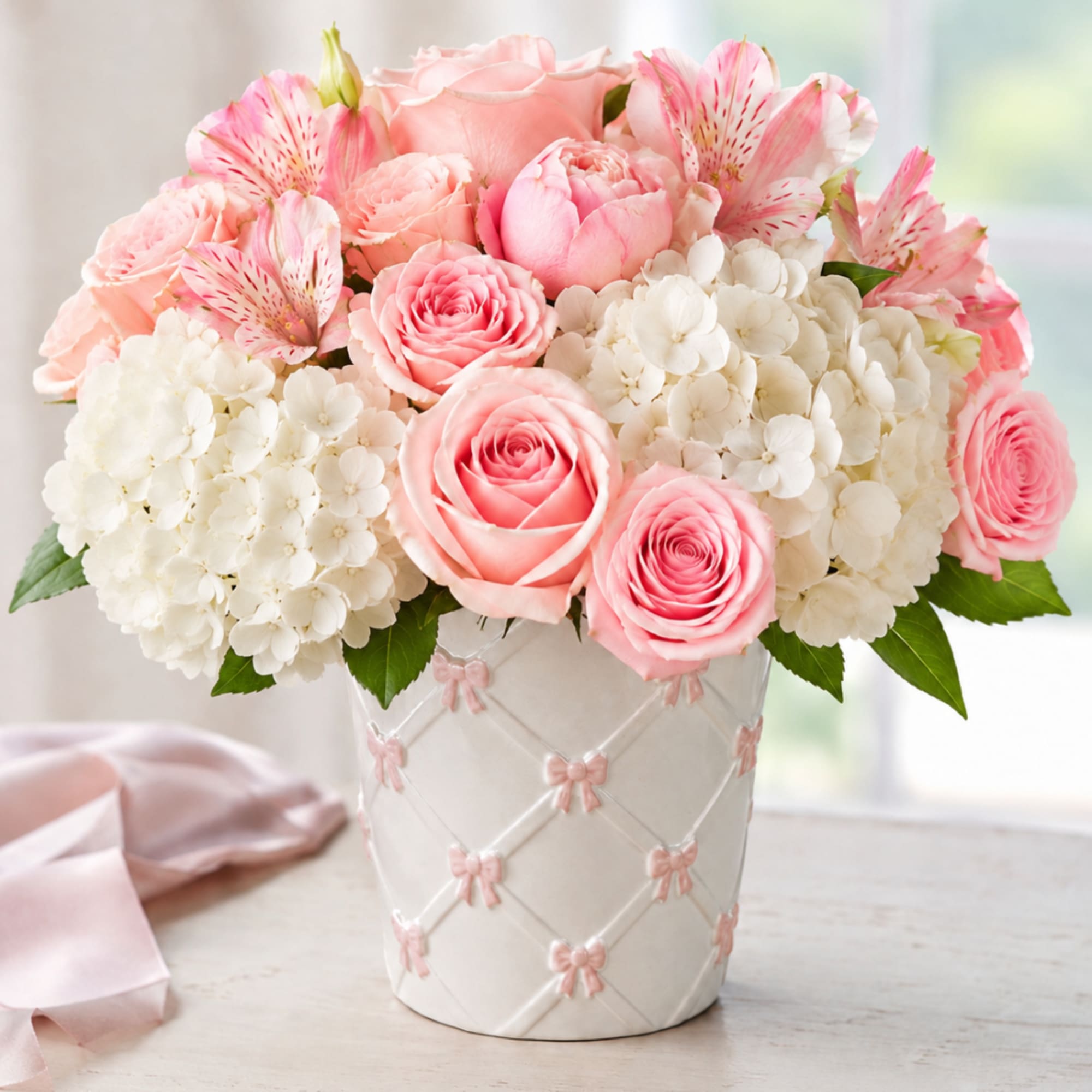 Pink roses and white hydrangeas in a white vase with pink bows