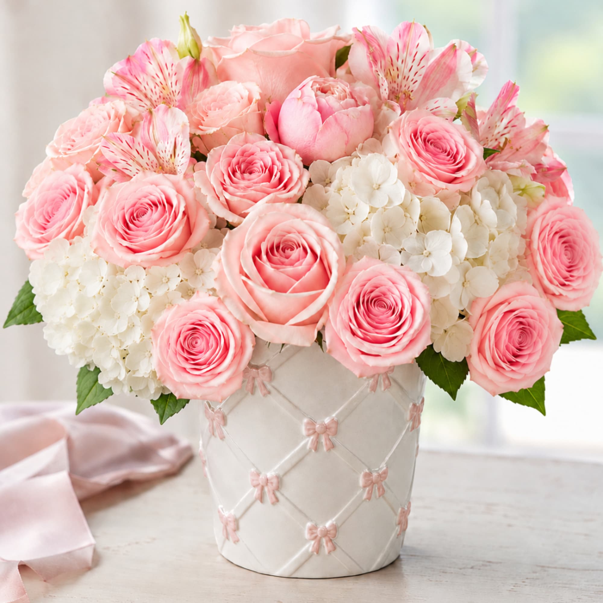 Pink roses and white hydrangeas in a white vase with pink bows