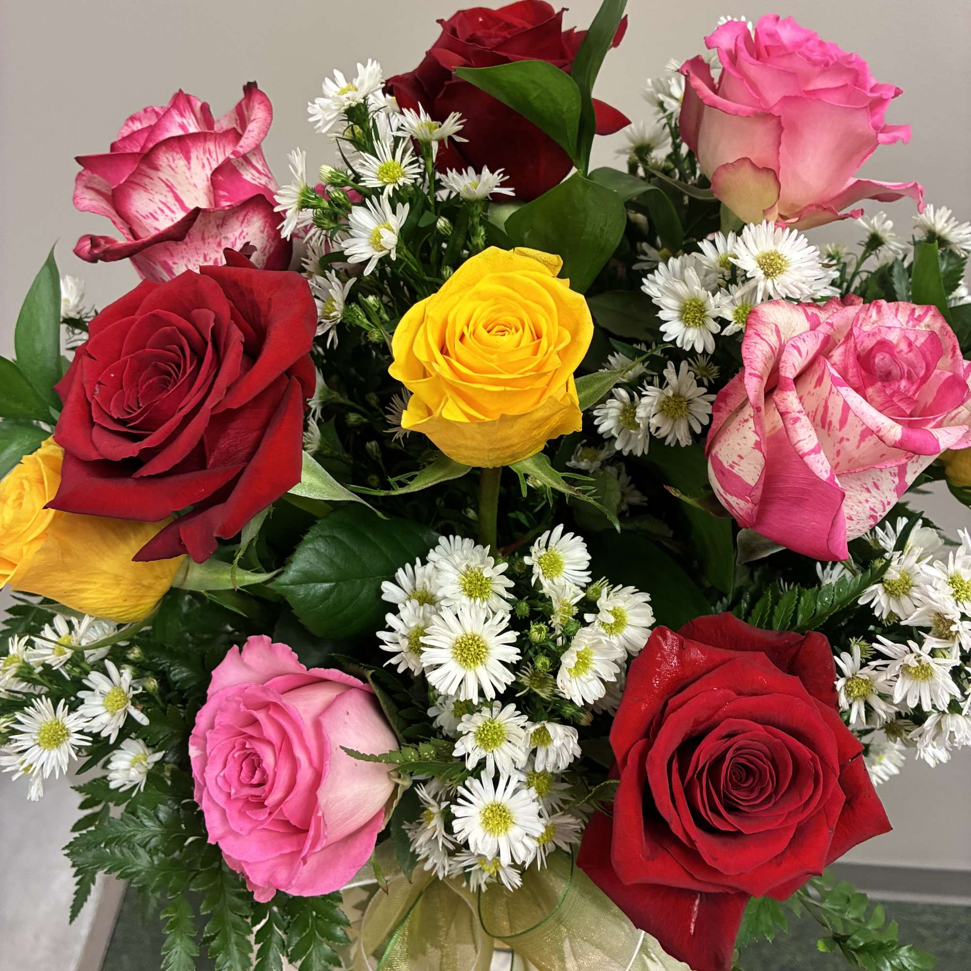 Bouquet of red, pink, and yellow roses with small white daisies